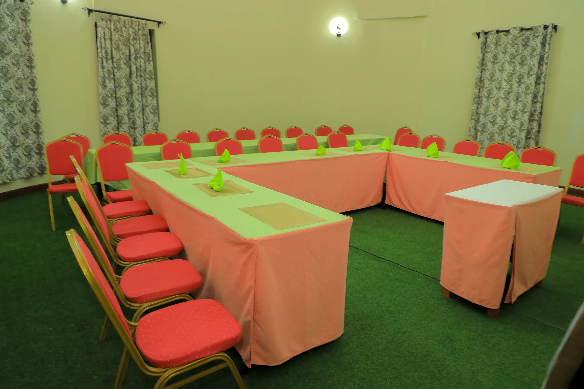 A meeting room with tables in a U-shape under peach cloths and red conference chairs