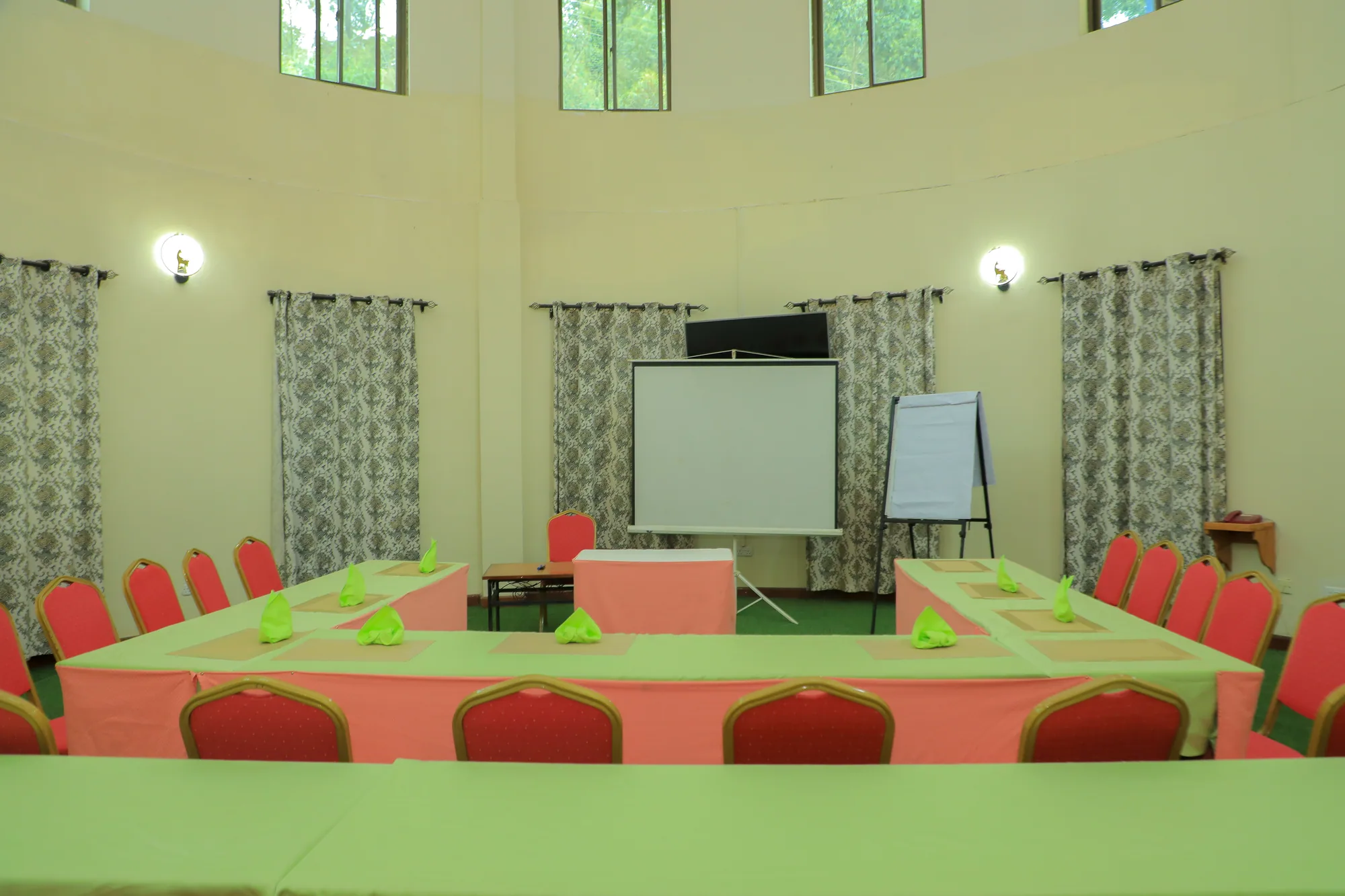 A conference room set in a hollow square with green cloths, a projector screen and flip chart