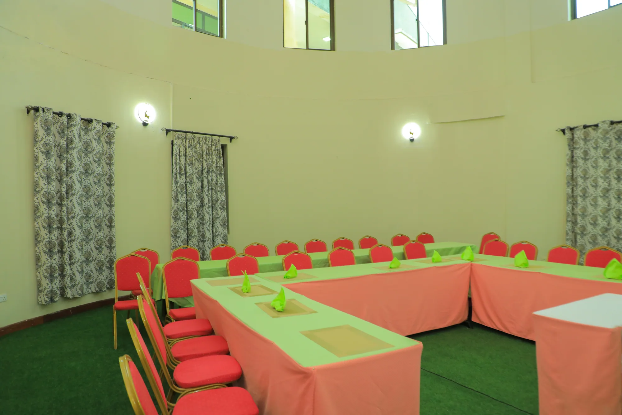 The conference room from the corner, peach-clothed tables and stacked red chairs