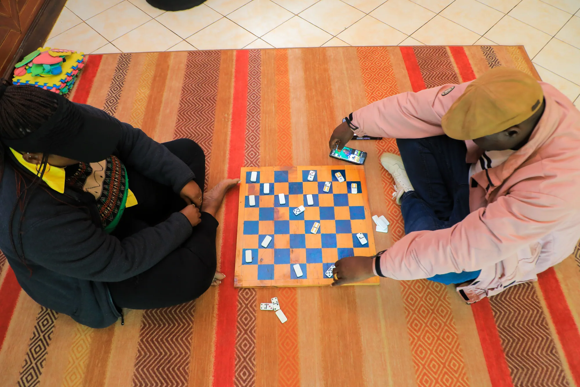 Two people playing draughts on a striped rug, seen from above