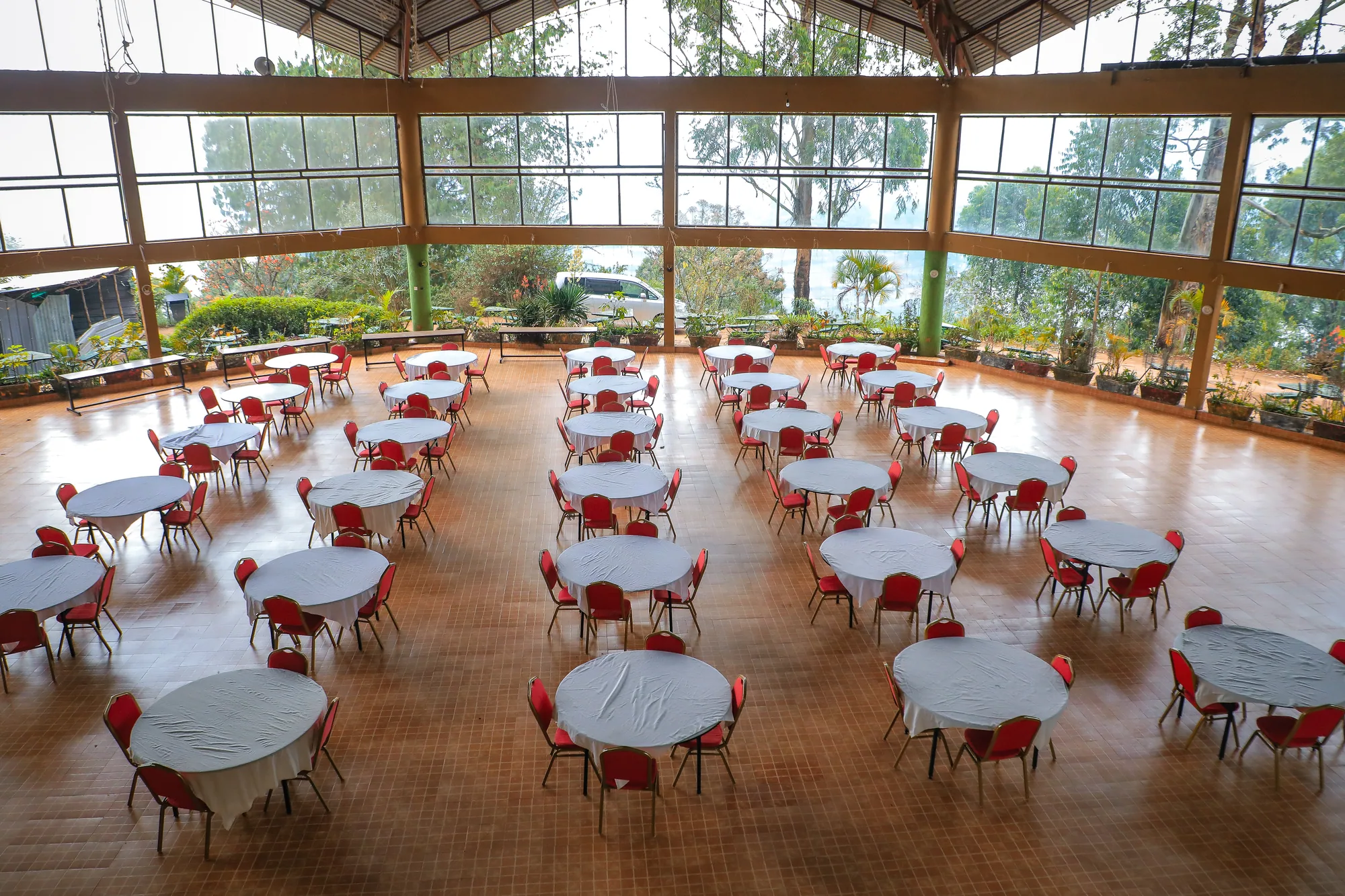 The glass-walled events hall set with round white tables and red chairs, hills beyond