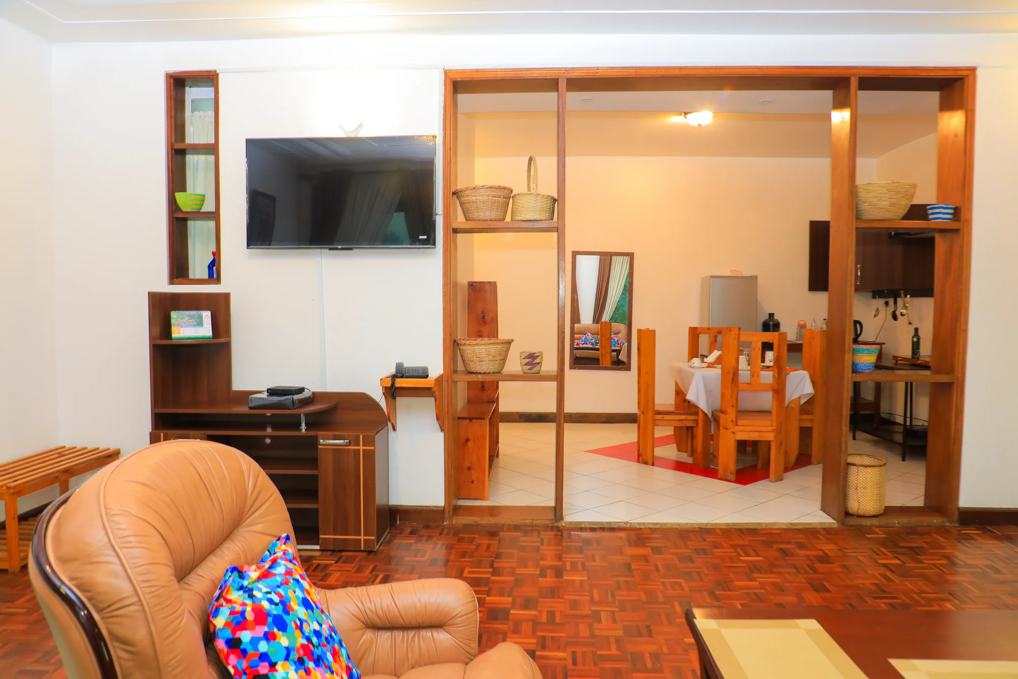 A suite sitting area with leather armchairs and a wall-mounted television, looking through to the dining space