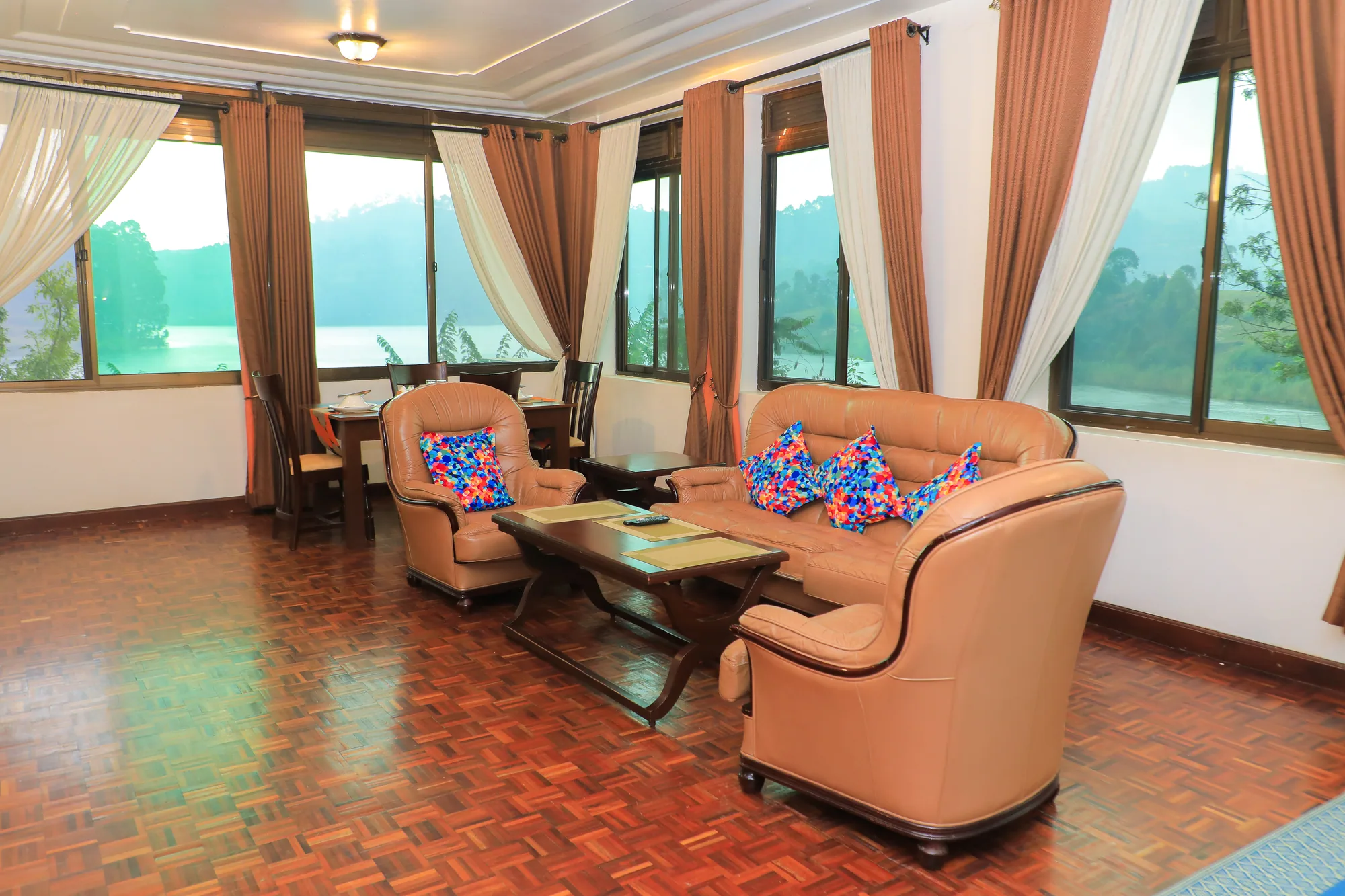A suite lounge with peach armchairs and a low table on a red tiled floor by the windows