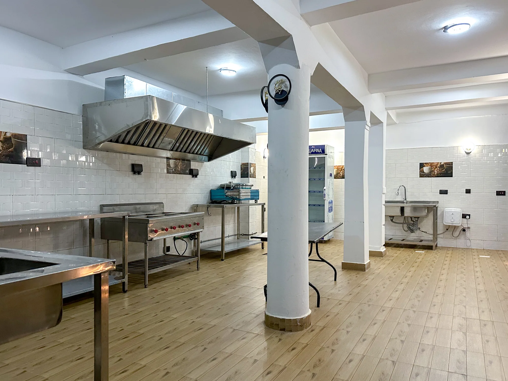A commercial kitchen with stainless steel benches, extraction hood and white pillars