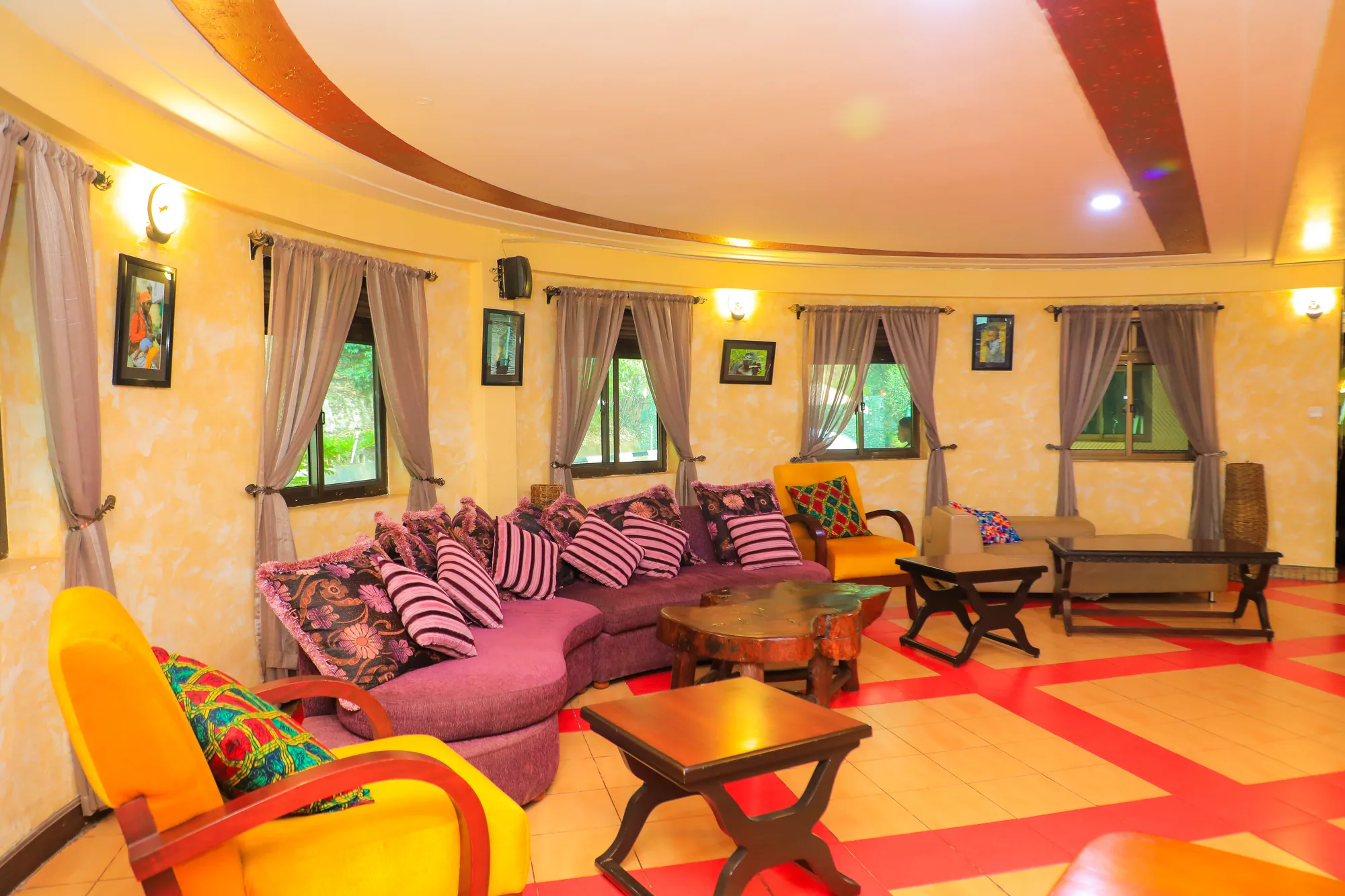 A lounge with purple sofas, timber stools and small windows under a moulded ceiling