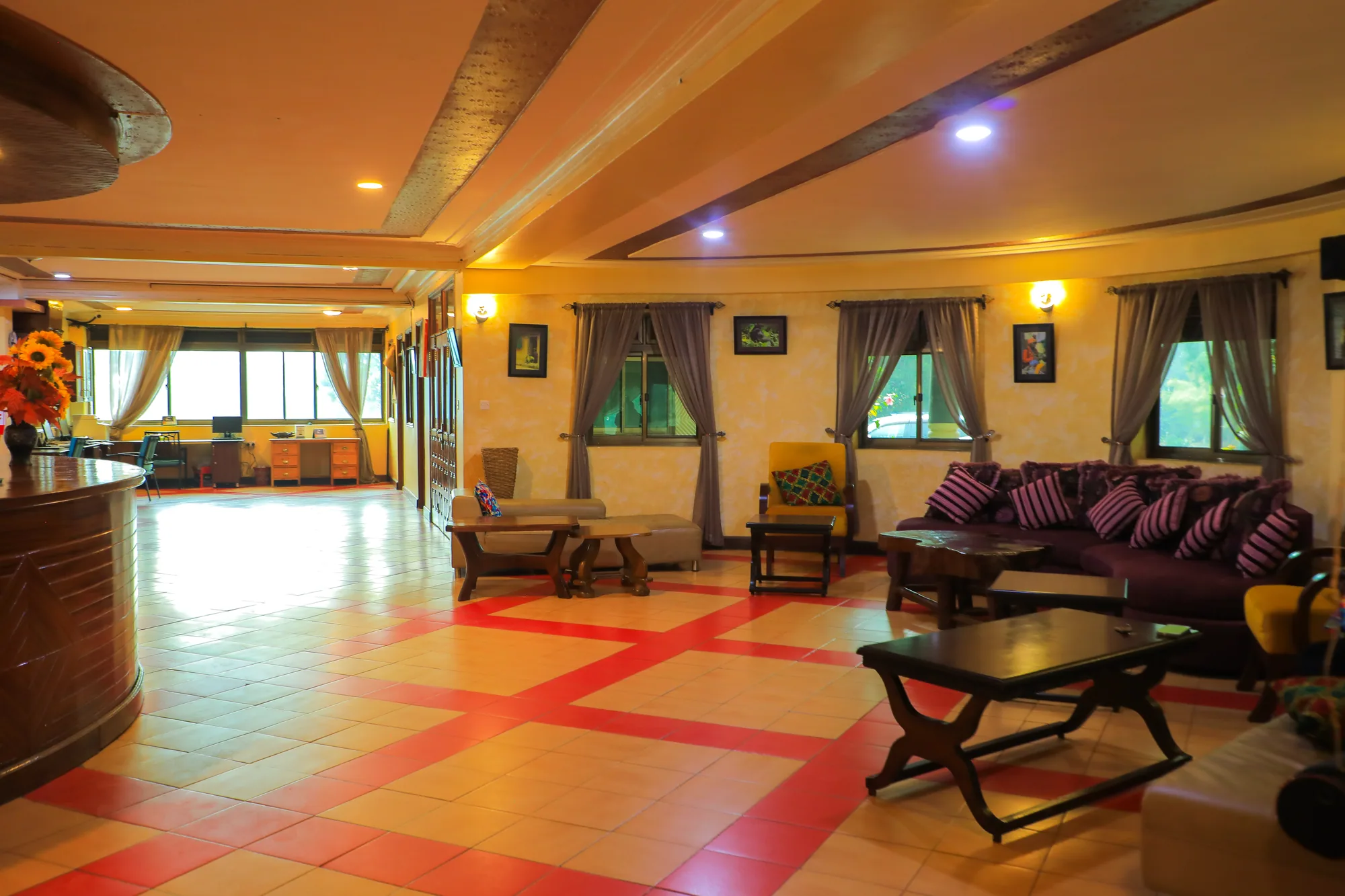 A wide lounge with purple sofas, timber tables and a red patterned tiled floor