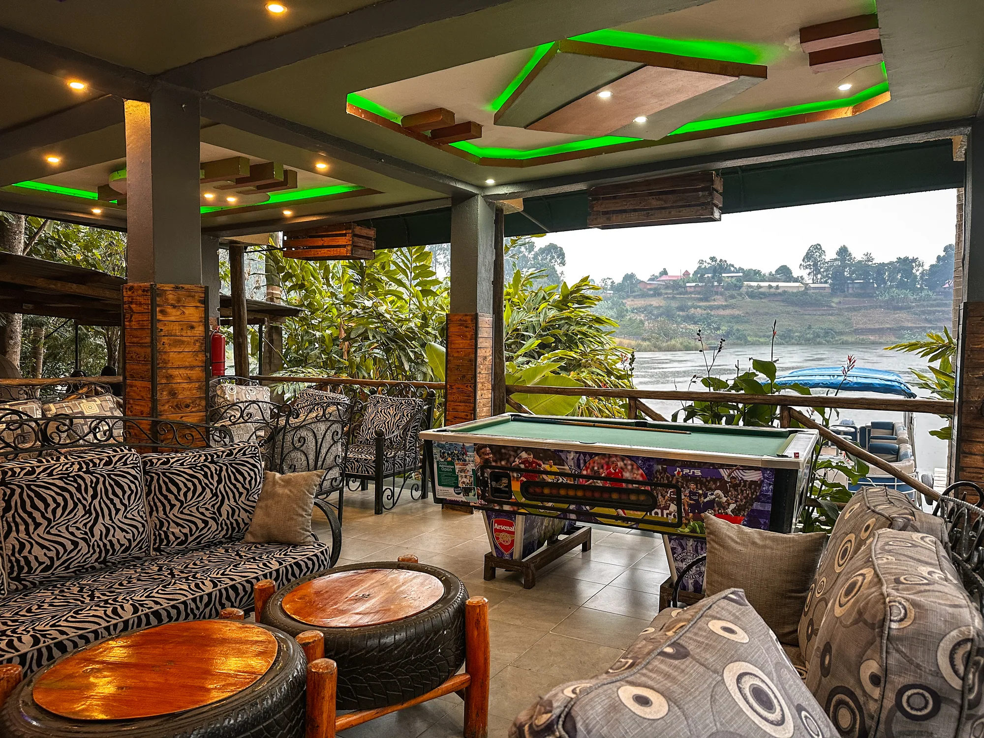 The games lounge with green ceiling lighting, patterned sofas and a pool table beside the lake