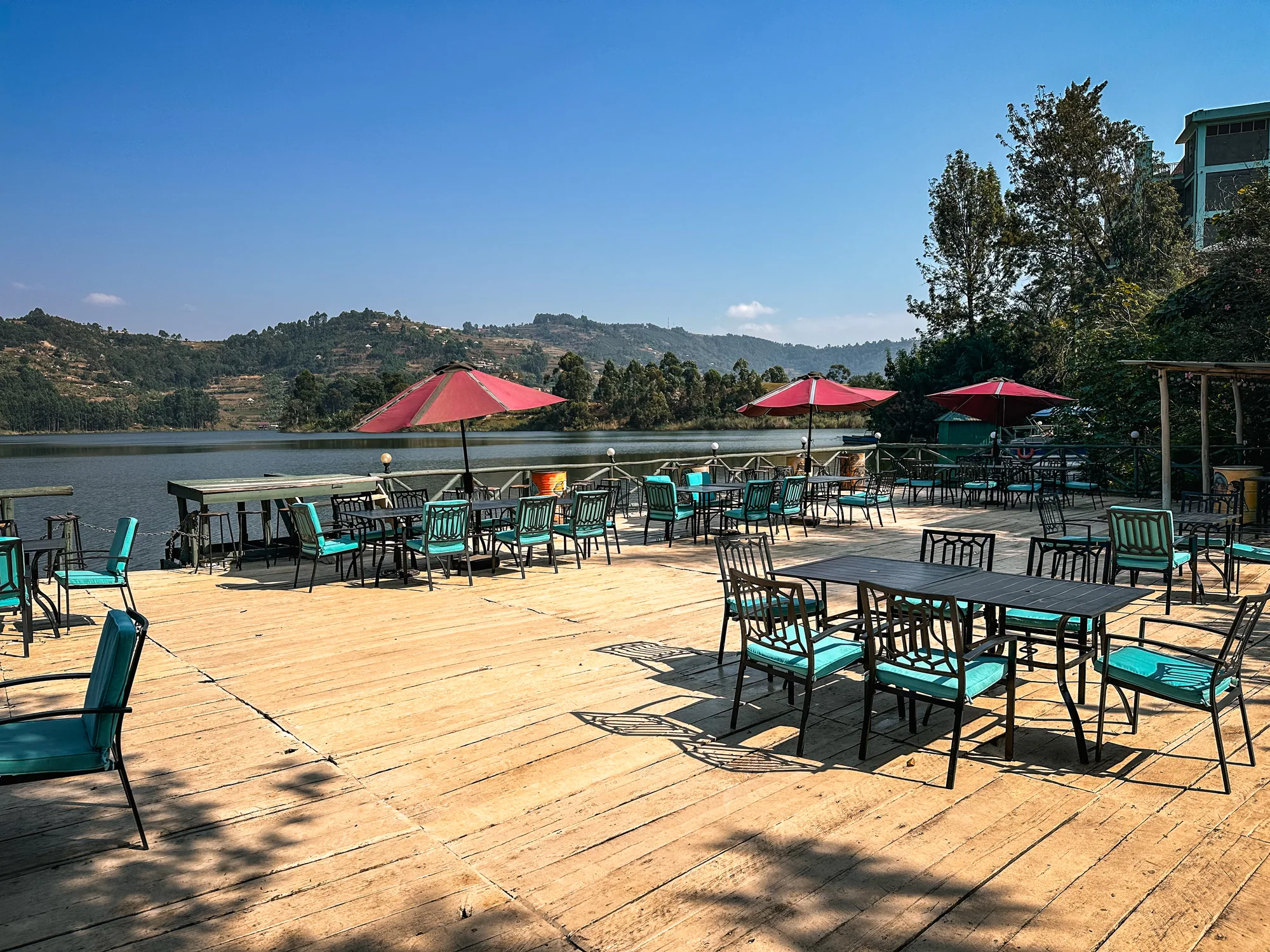 The deck laid with tables and turquoise chairs under red parasols beside the lake