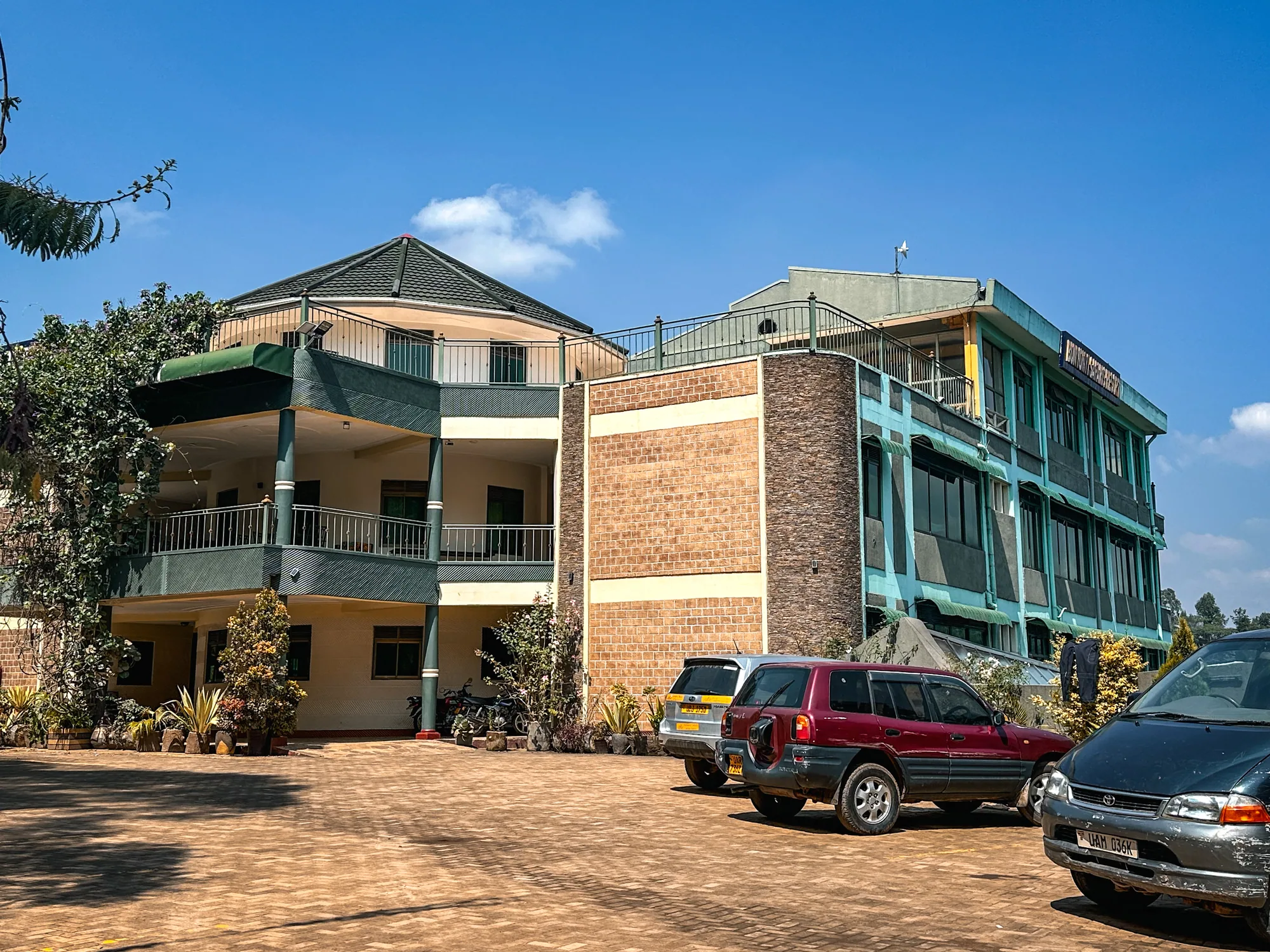 The brick and cream guest block with balconies and cars parked on the earth forecourt