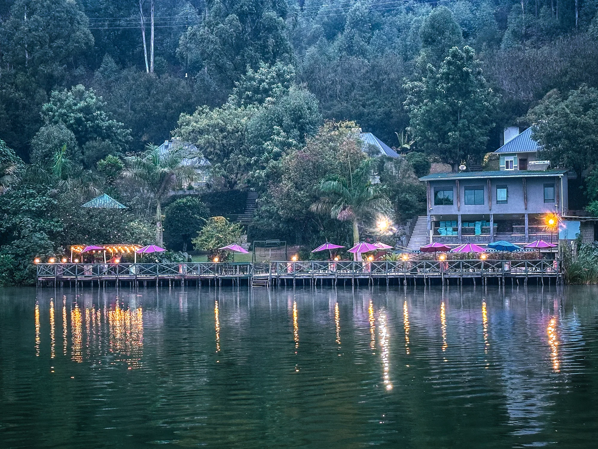 The lit lakeside decks and pink parasols of the resort reflected in the water at dusk