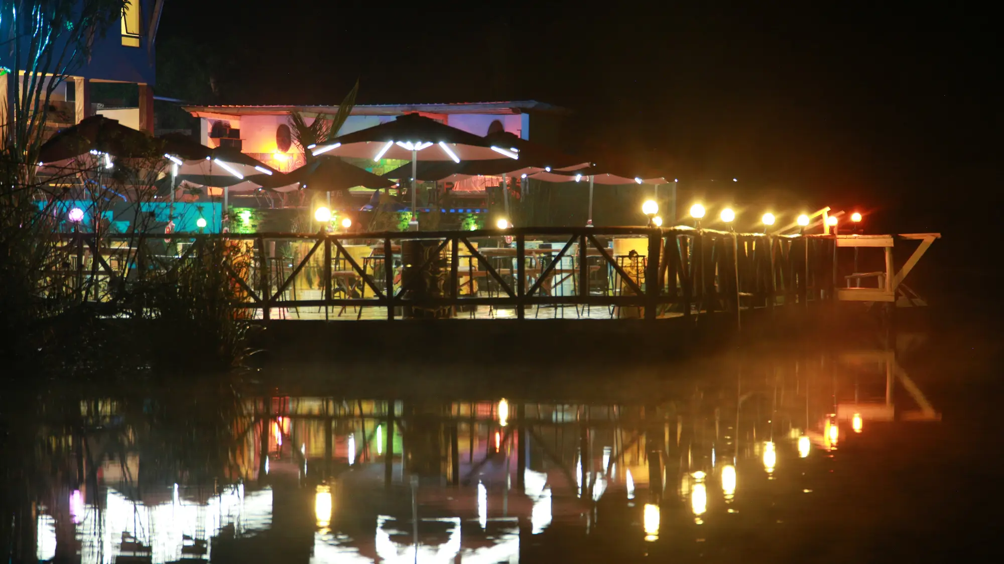 Lakeside deck strung with lights, reflected in the water at night