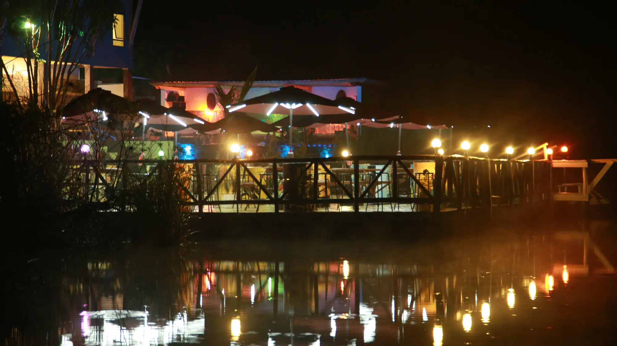 Lit lakeside deck and parasols reflected in the lake after dark