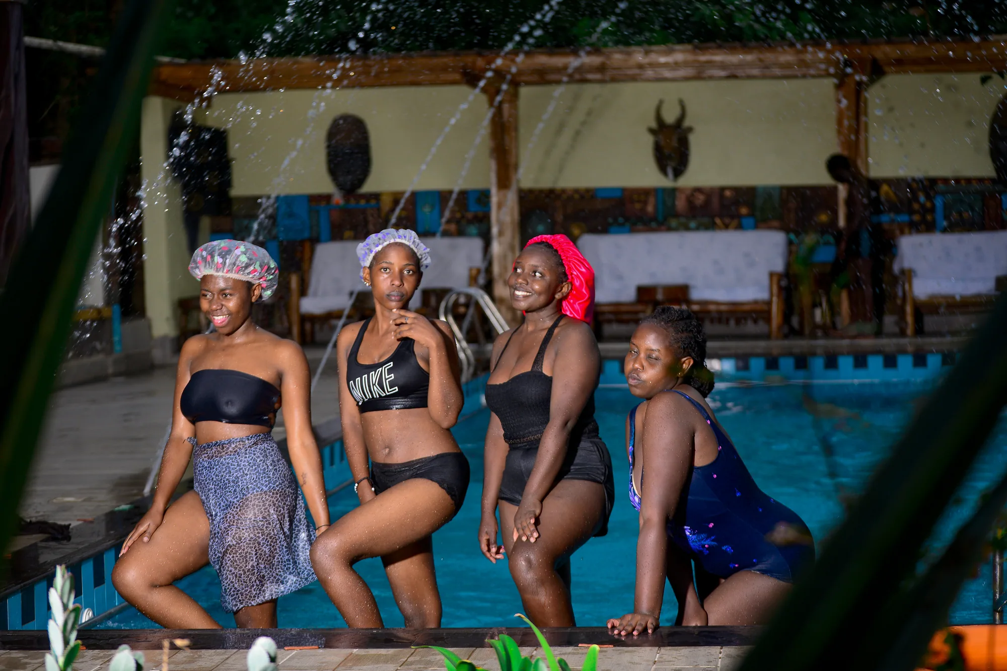Four guests in swimwear and swim caps standing at the poolside in the evening