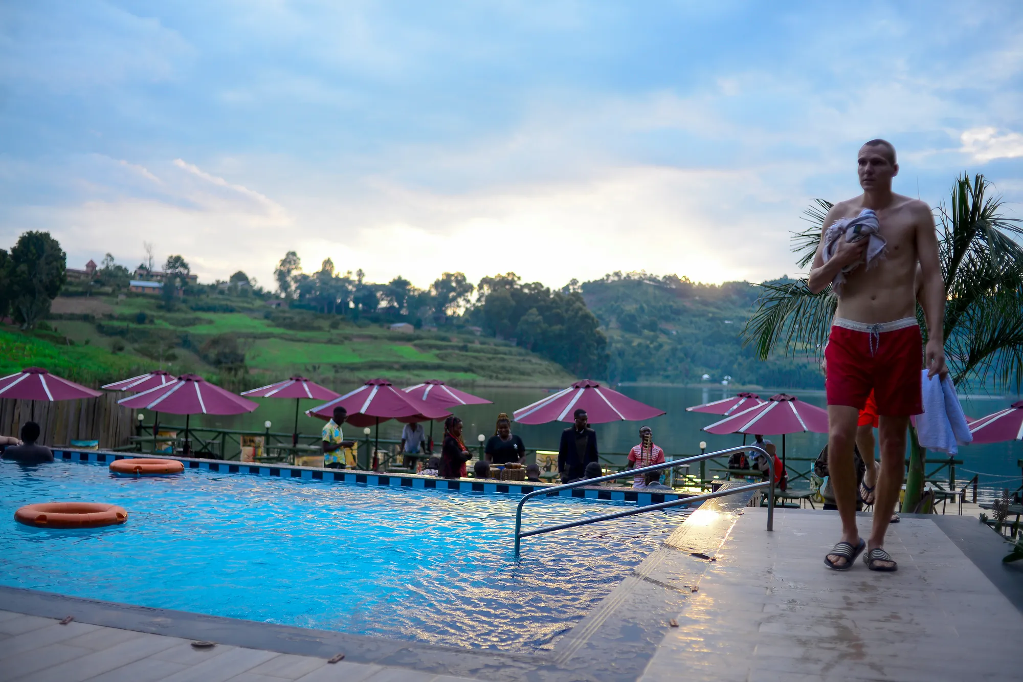 A guest standing at the poolside against a bright sky with the parasols behind