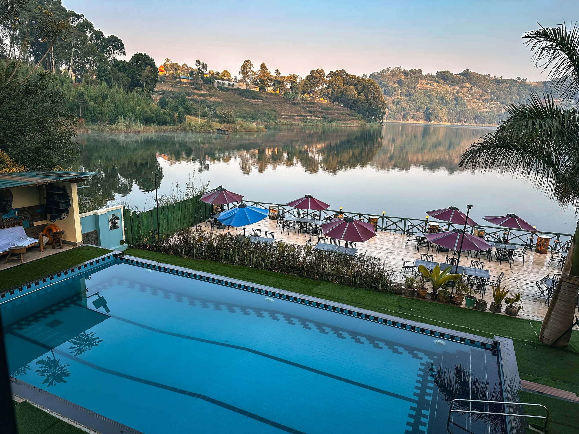 The pool on its lawn terrace with the lake mirror-calm at dawn behind