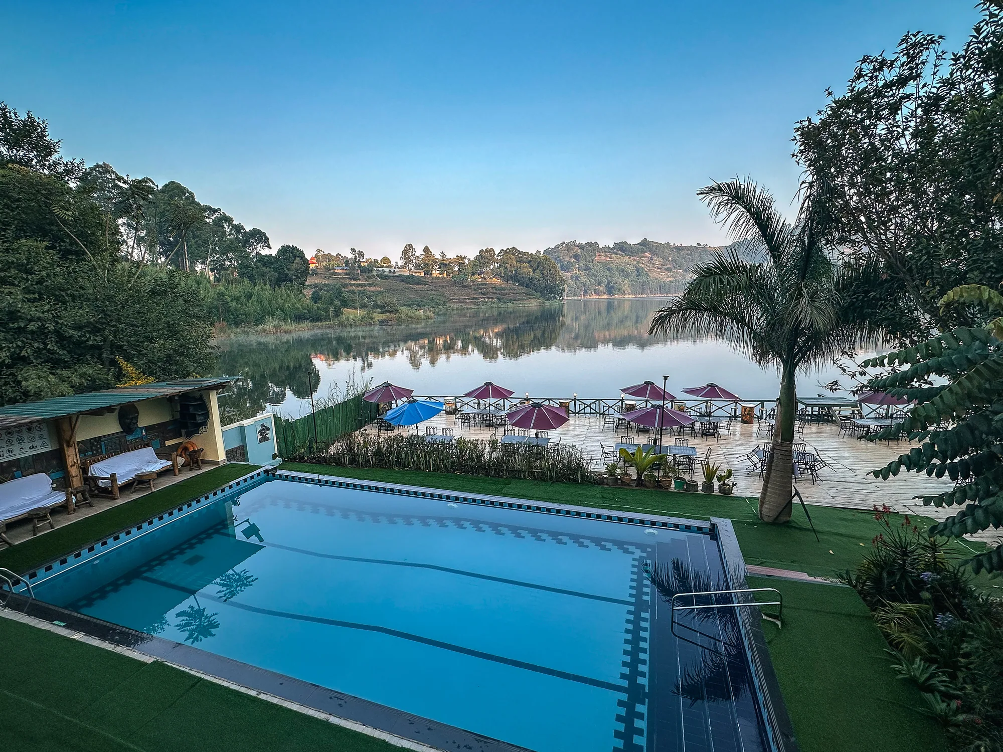 The pool with a palm beside it and the still lake and pink parasols beyond