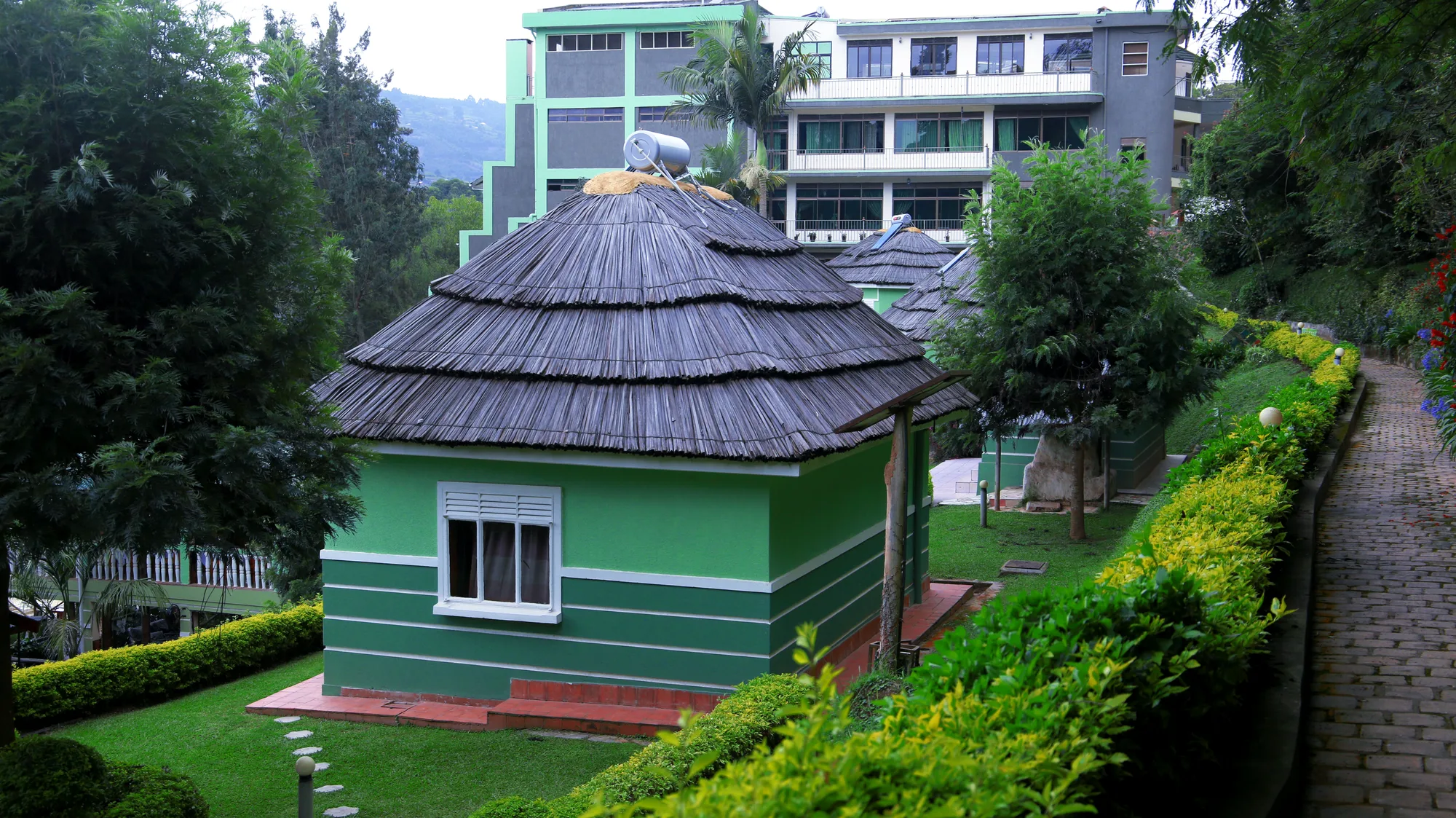 A thatched green cottage among trimmed hedges with the main hotel building and hills behind