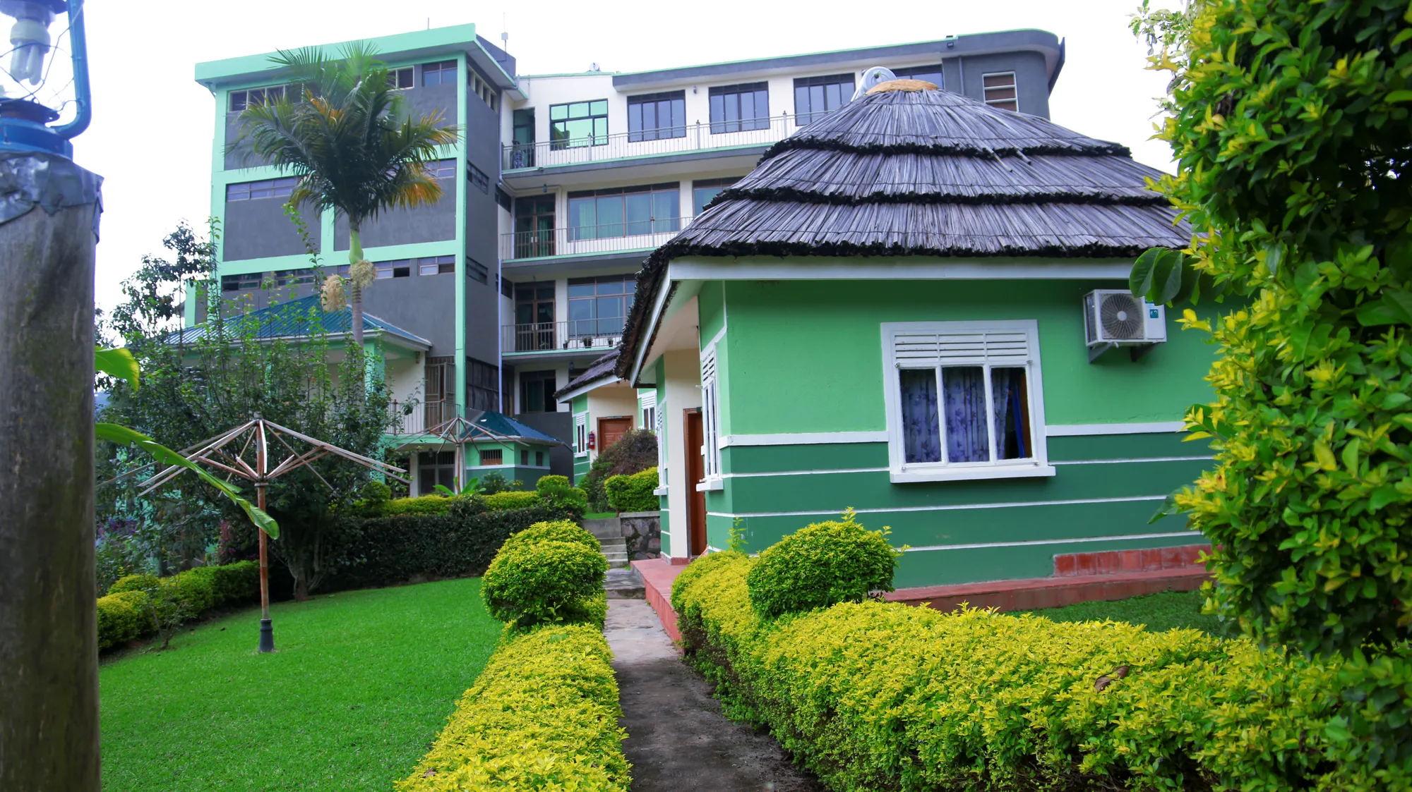 Thatched green cottages along a paved garden path with the main hotel building behind