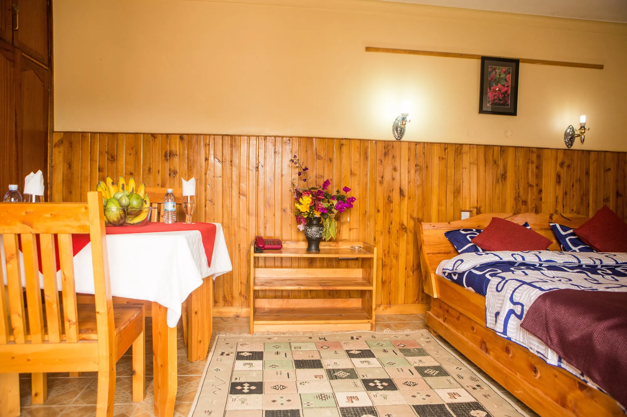 A timber-panelled room with a bed, a small dining table and chair and a tiled floor
