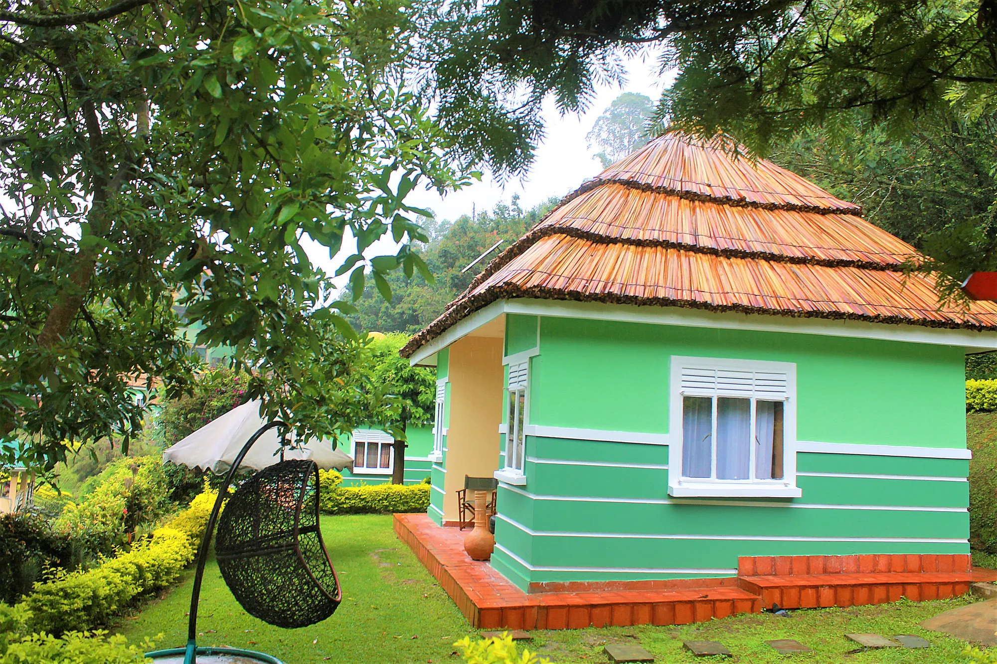 A green cottage with a shingled conical roof and a hanging egg chair on the lawn outside