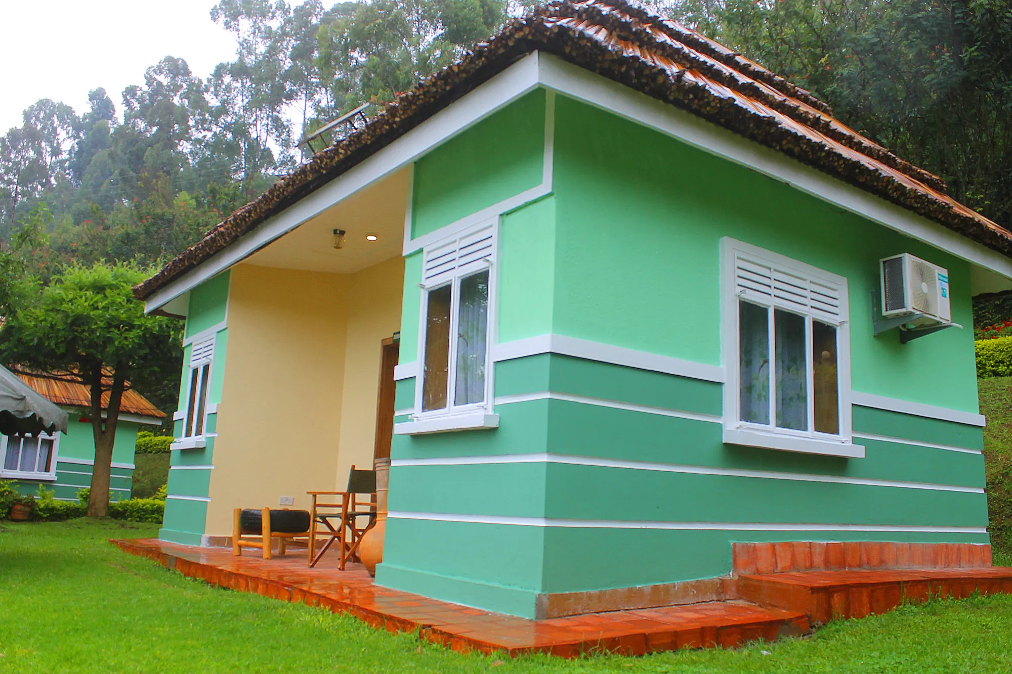 A green cottage with white-framed windows and a small table and chairs at the corner