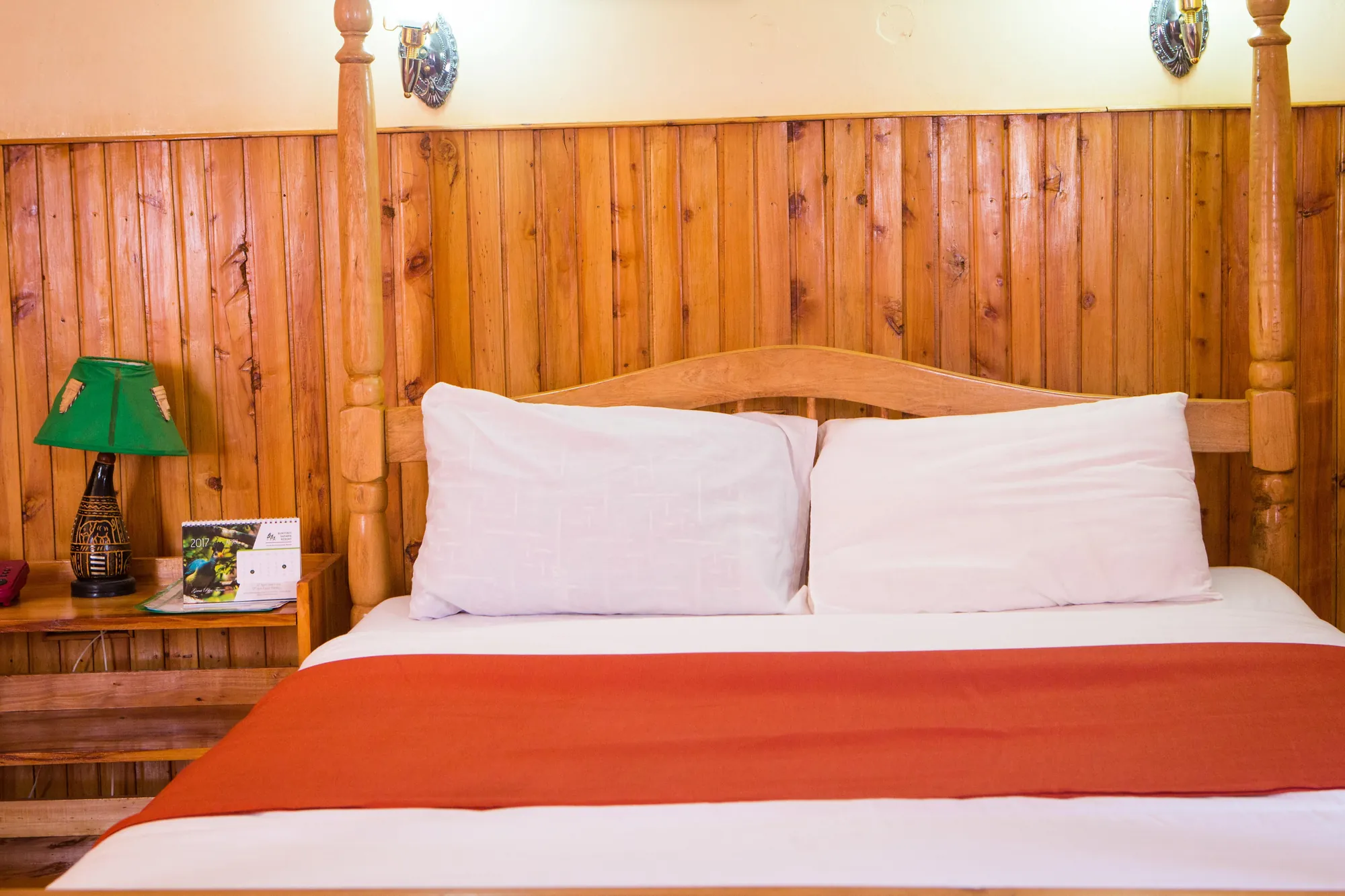 Double / Twin Room: double bed with white pillows and a red runner against a timber-panelled wall with a green lamp