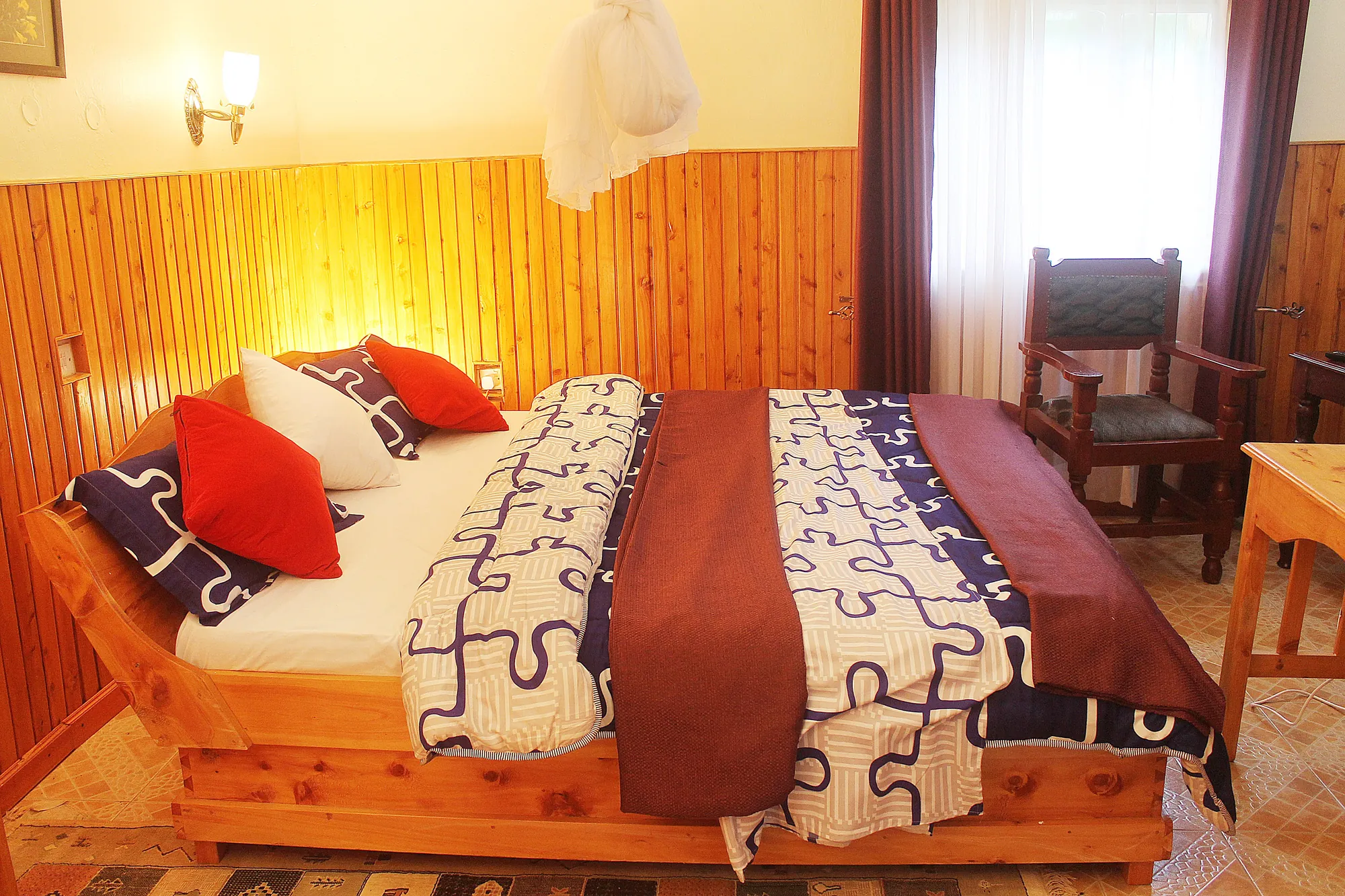 Double / Twin Room: double bed with a patterned throw and red cushions in a timber-panelled room