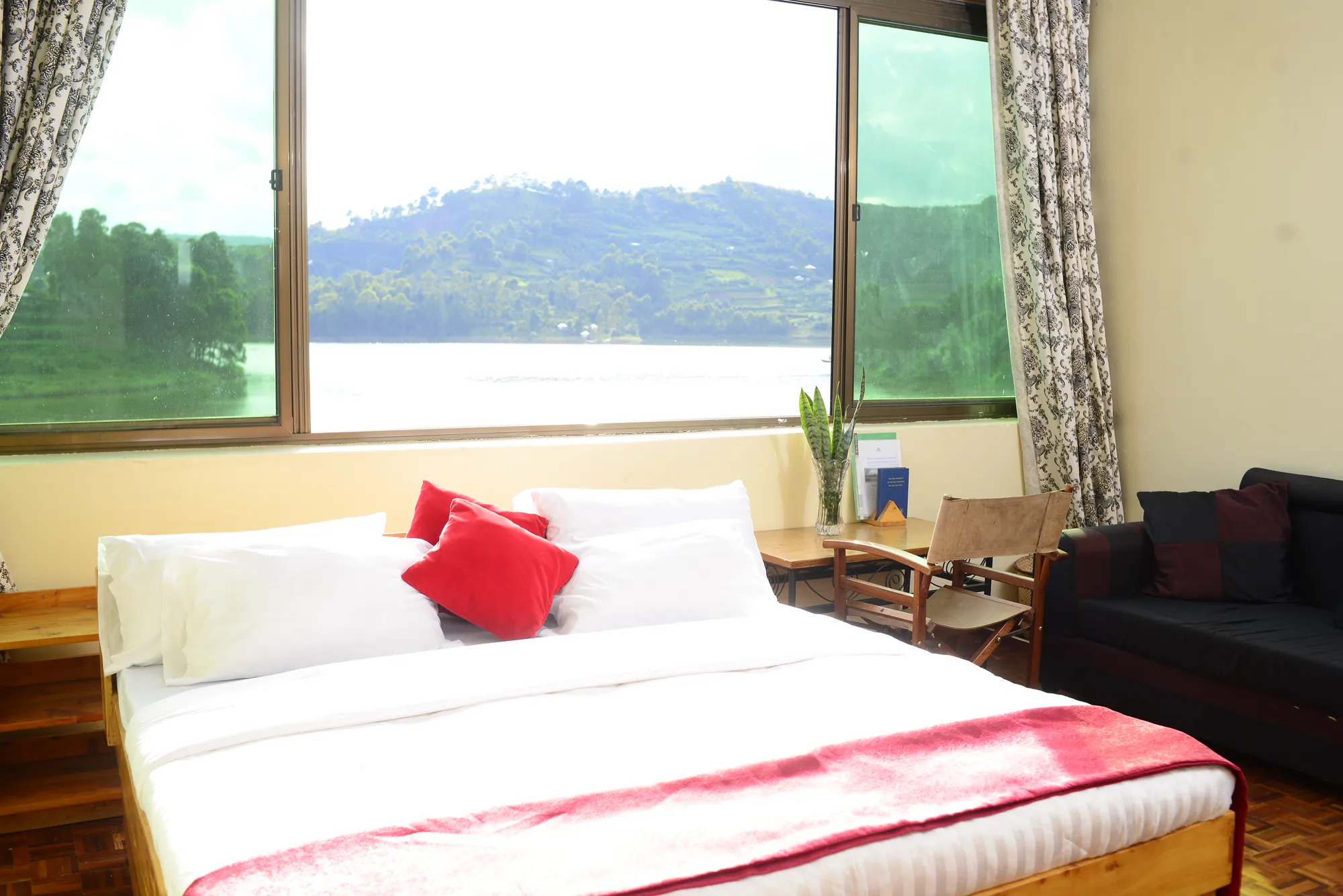 Double / Twin Room: bed with a red runner beside a picture window over the lake, with a sofa alongside
