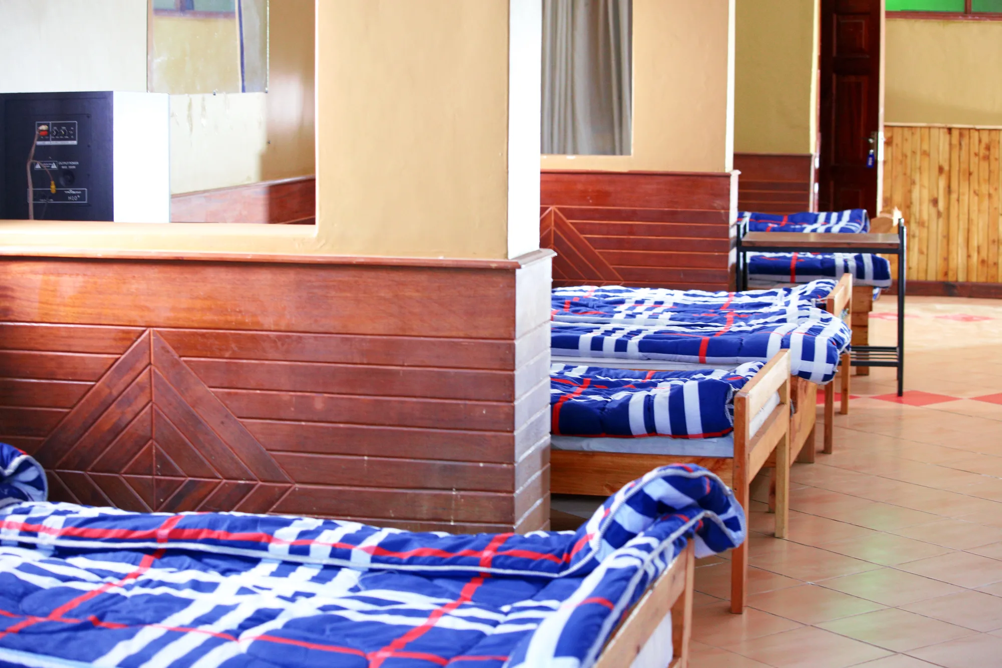 Dormitory: row of single dormitory beds with blue checked blankets along a timber partition