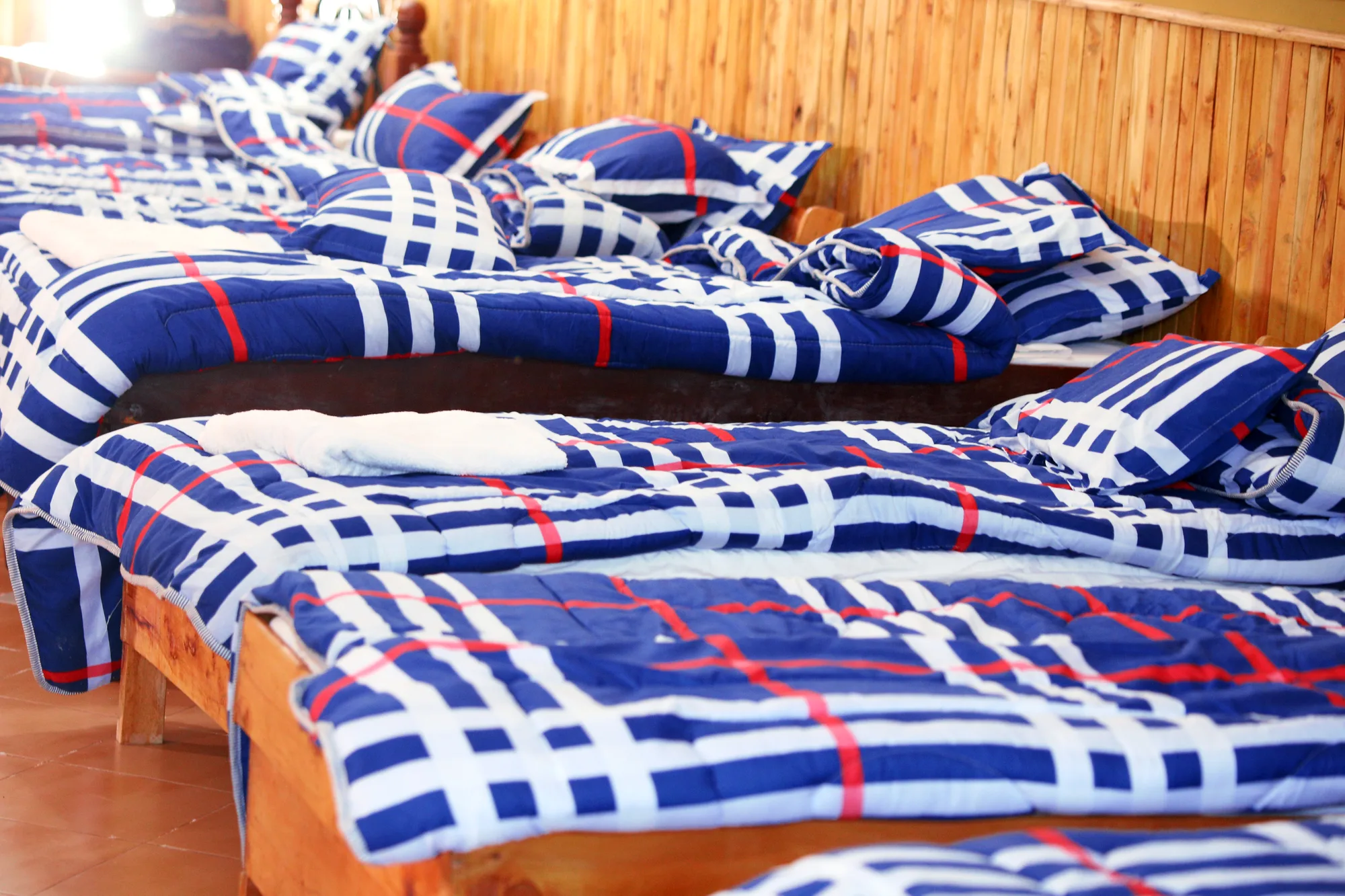 Dormitory: single dormitory beds made up with blue checked blankets and matching pillows beside a timber wall