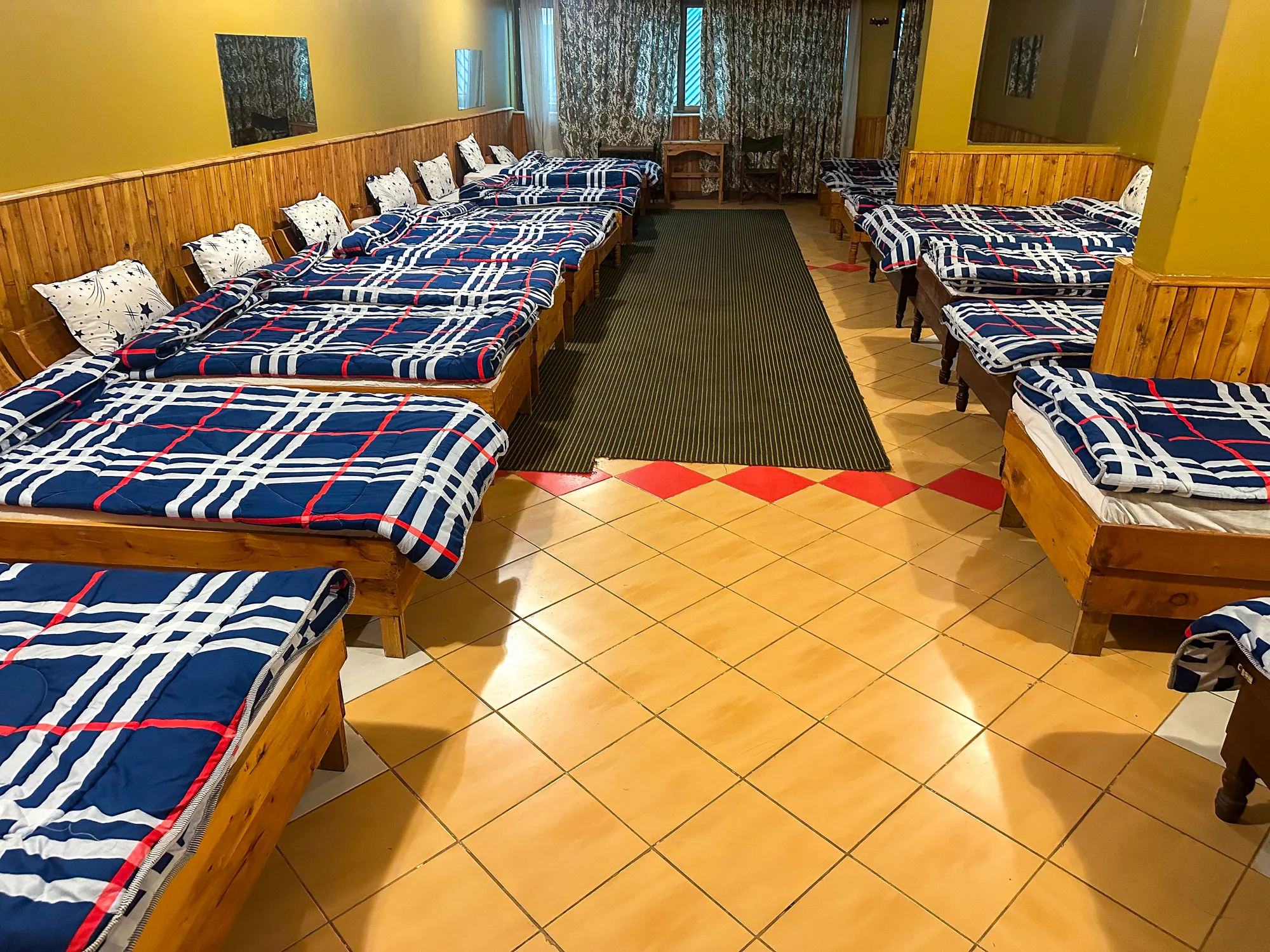 Dormitory rows of single beds with navy checked blankets along timber-panelled walls