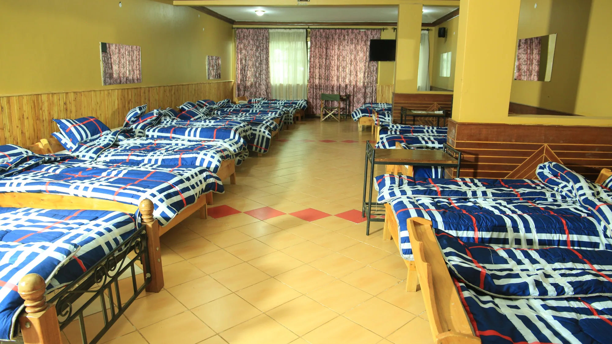 Dormitory beds in blue checked bedding lining the walls, with curtained windows at the end