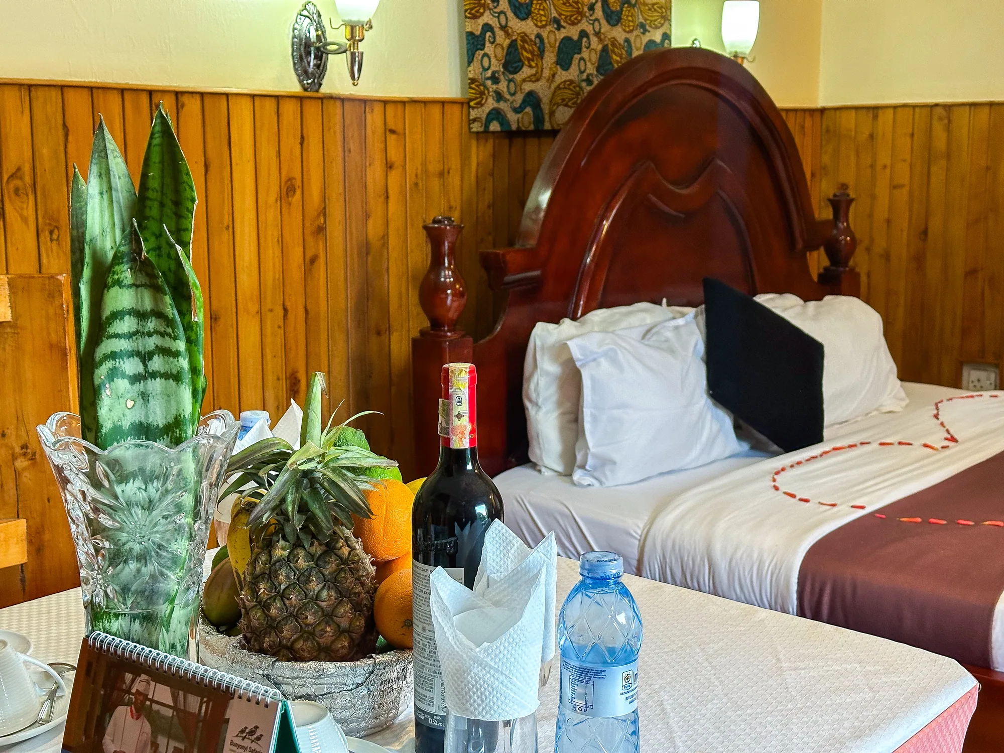 Cottage: bed with a carved timber headboard and a welcome table of fruit, wine and water in front