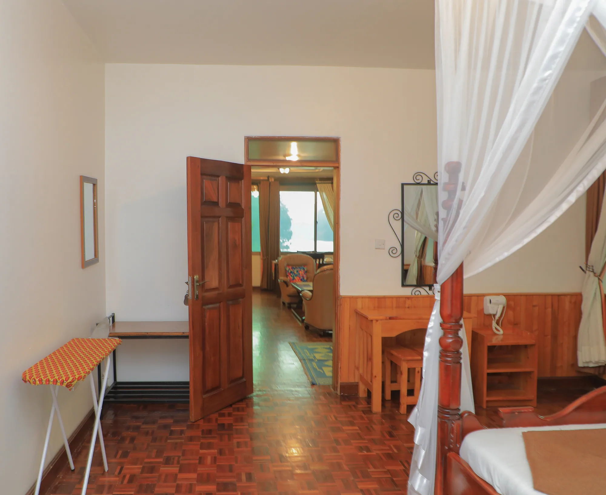 A room entrance with an open timber door, ironing board and a mosquito-netted bed beyond