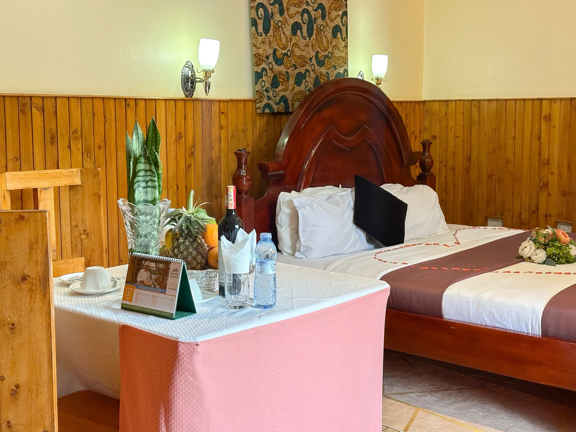 Cottage: carved-headboard bed with a welcome tray of fruit and wine on a pink-clothed table