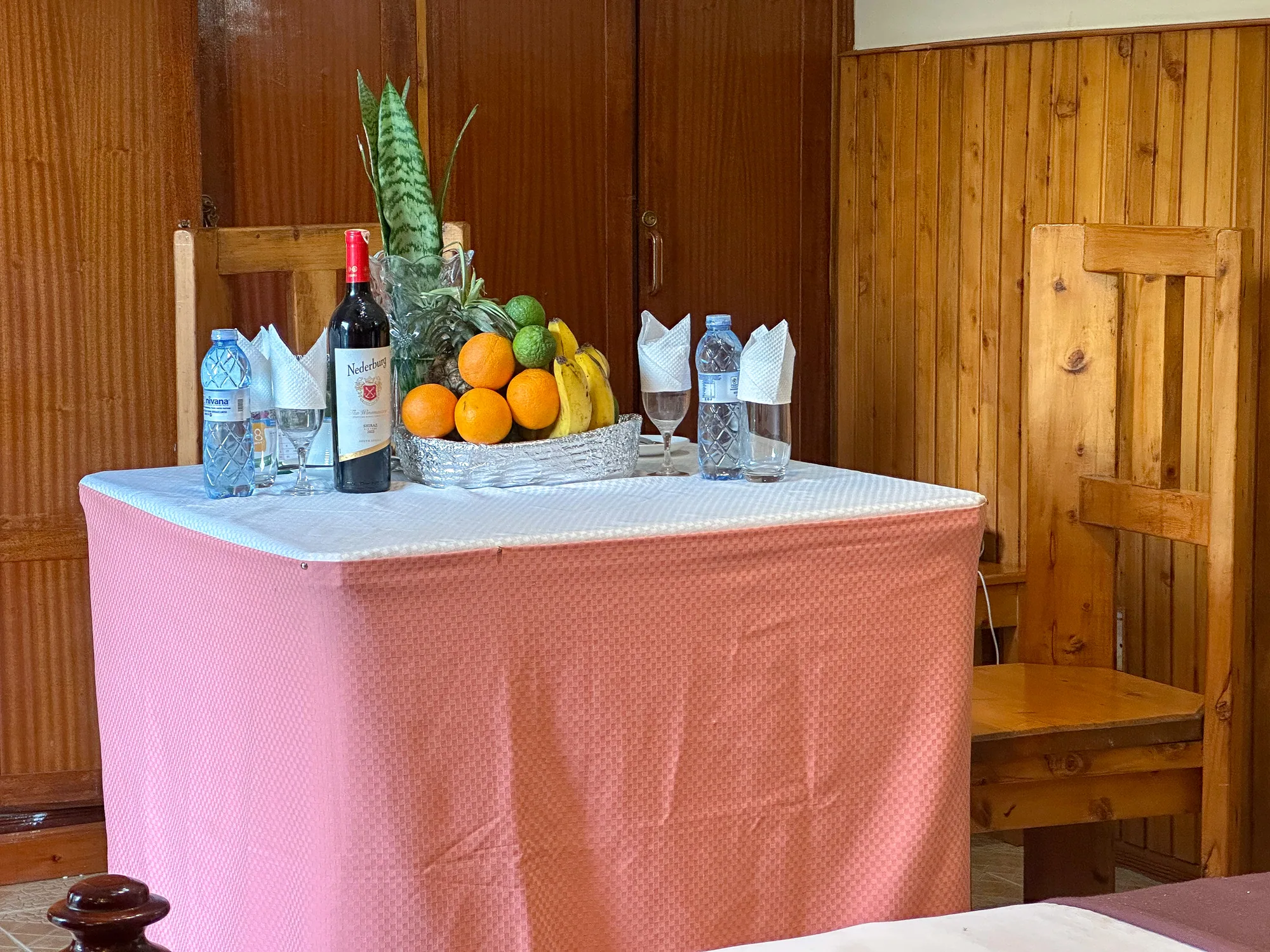 Cottage: welcome table with wine, bottled water, oranges and pineapple in a timber-panelled room