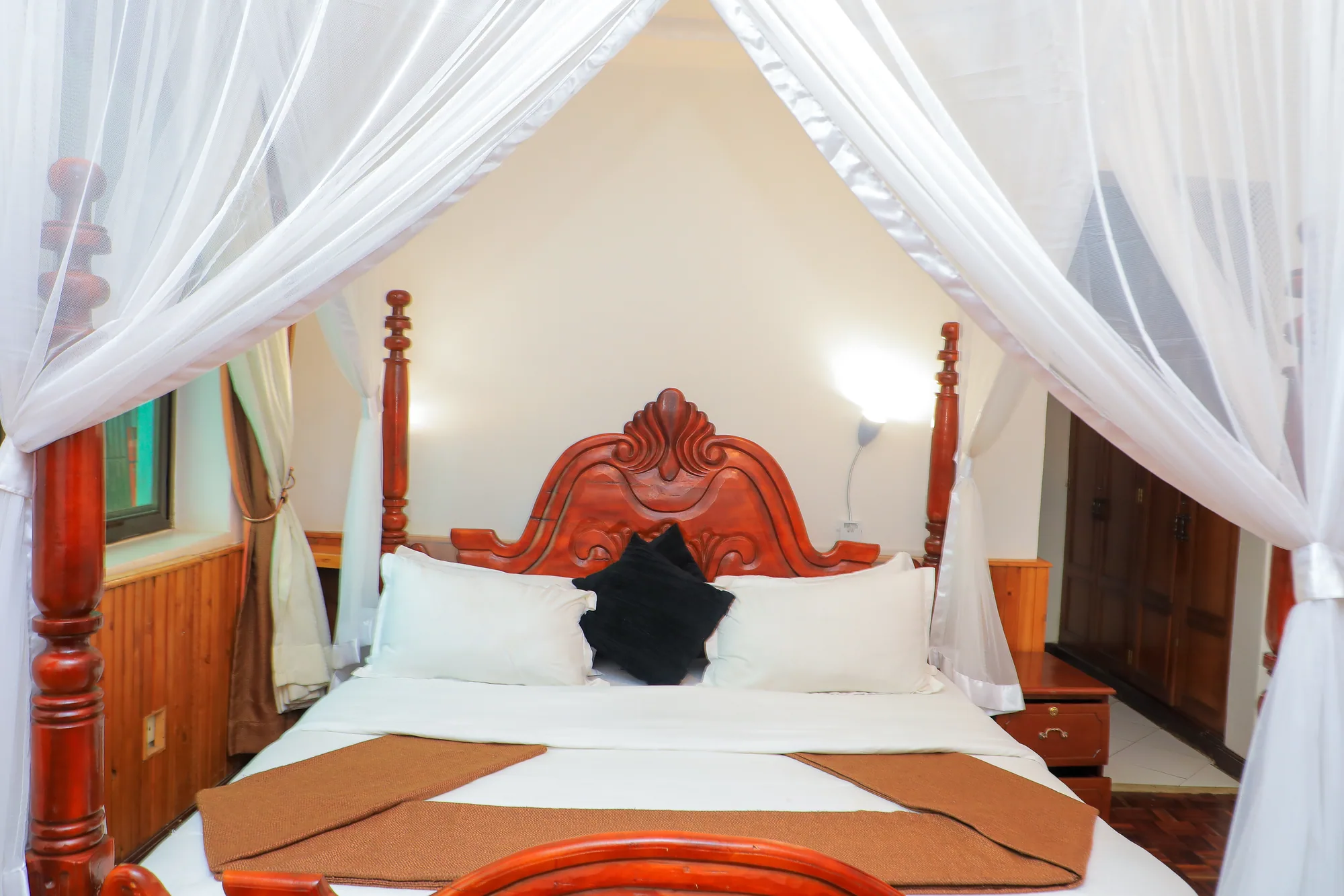 Cottage: carved bed under a full mosquito net with a maroon and cream runner