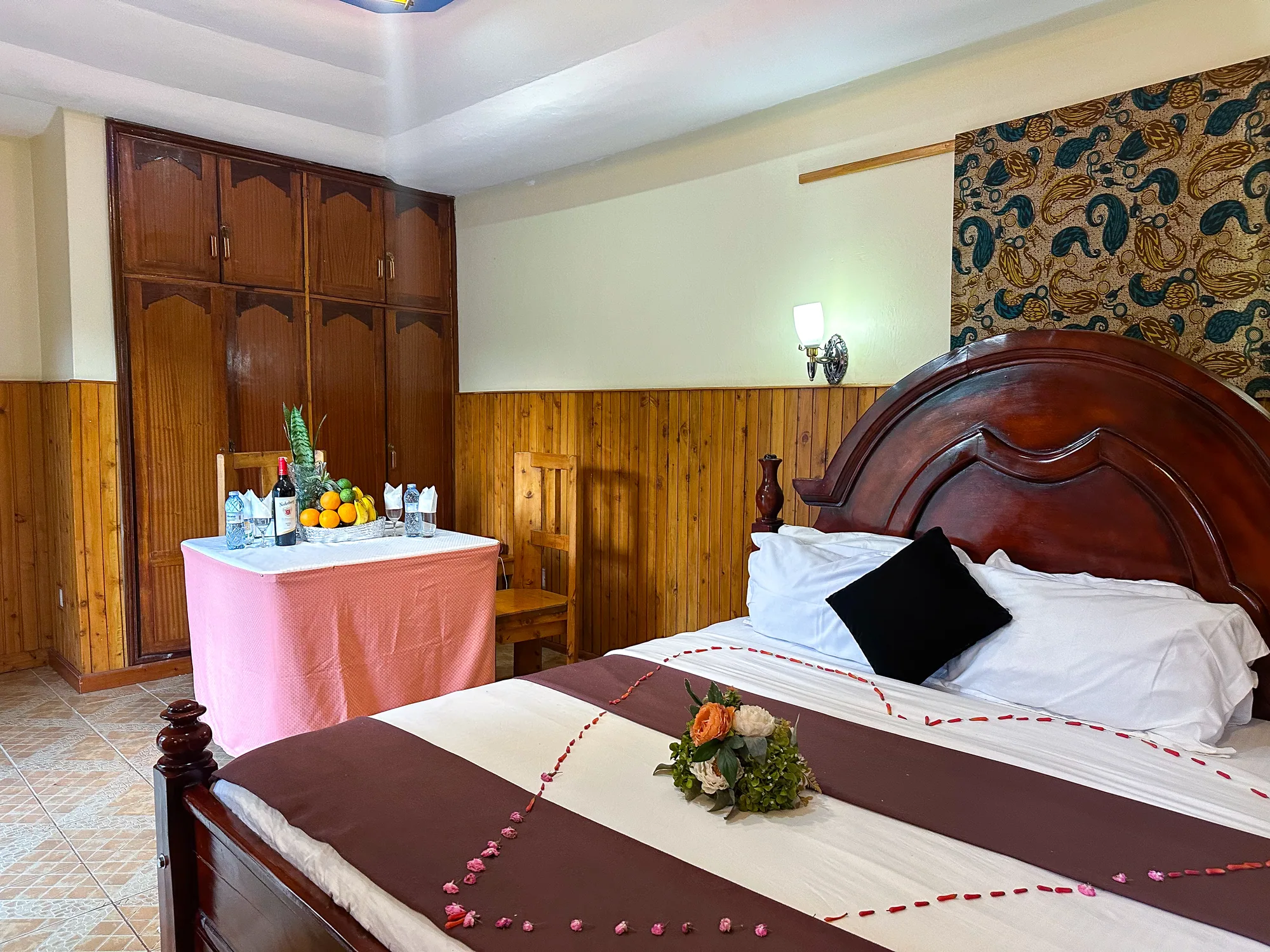 Cottage: bed with a carved headboard and a fruit and wine welcome table beside the wardrobe