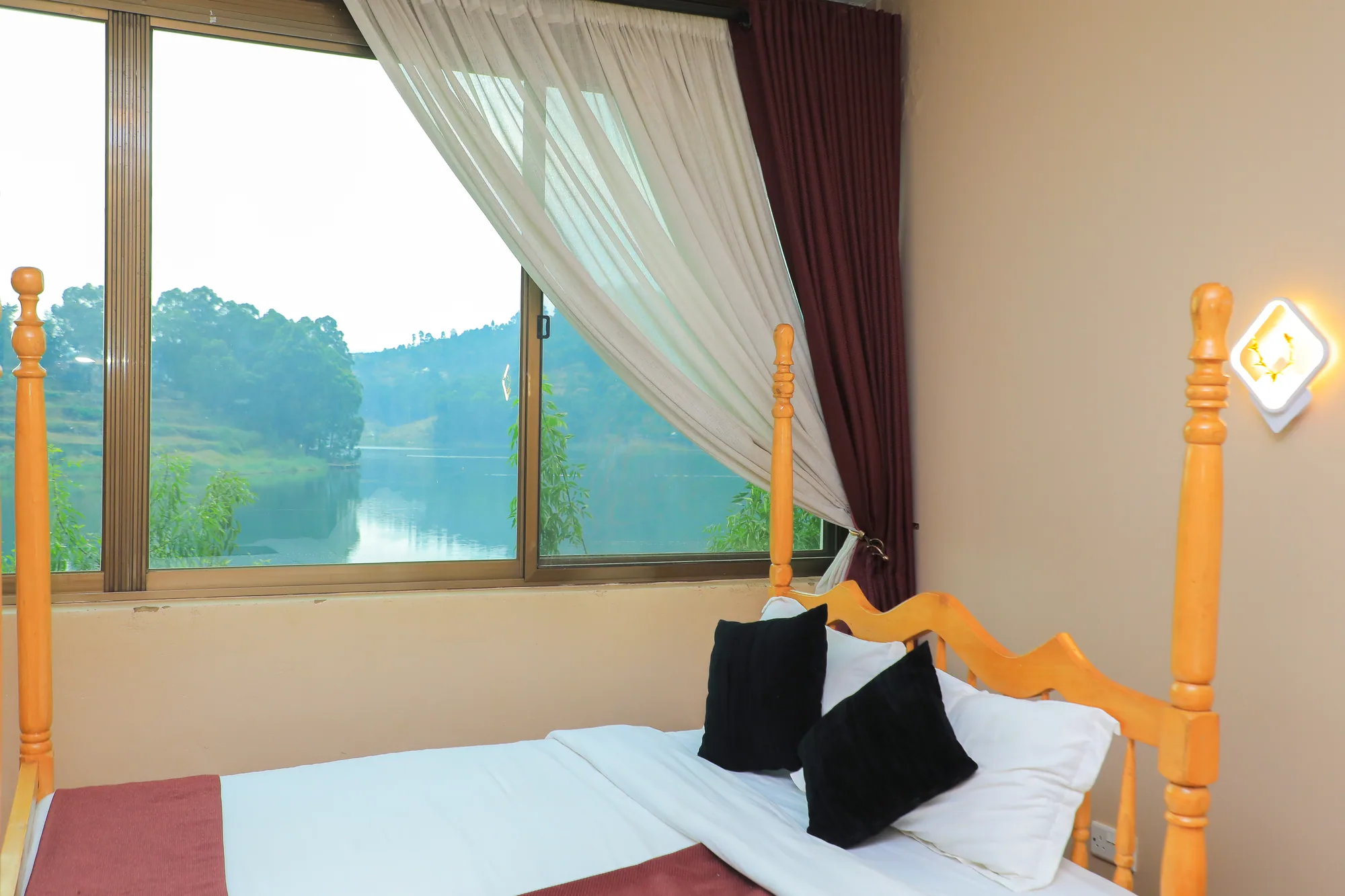 A bed with black cushions beside a corner window looking down the lake