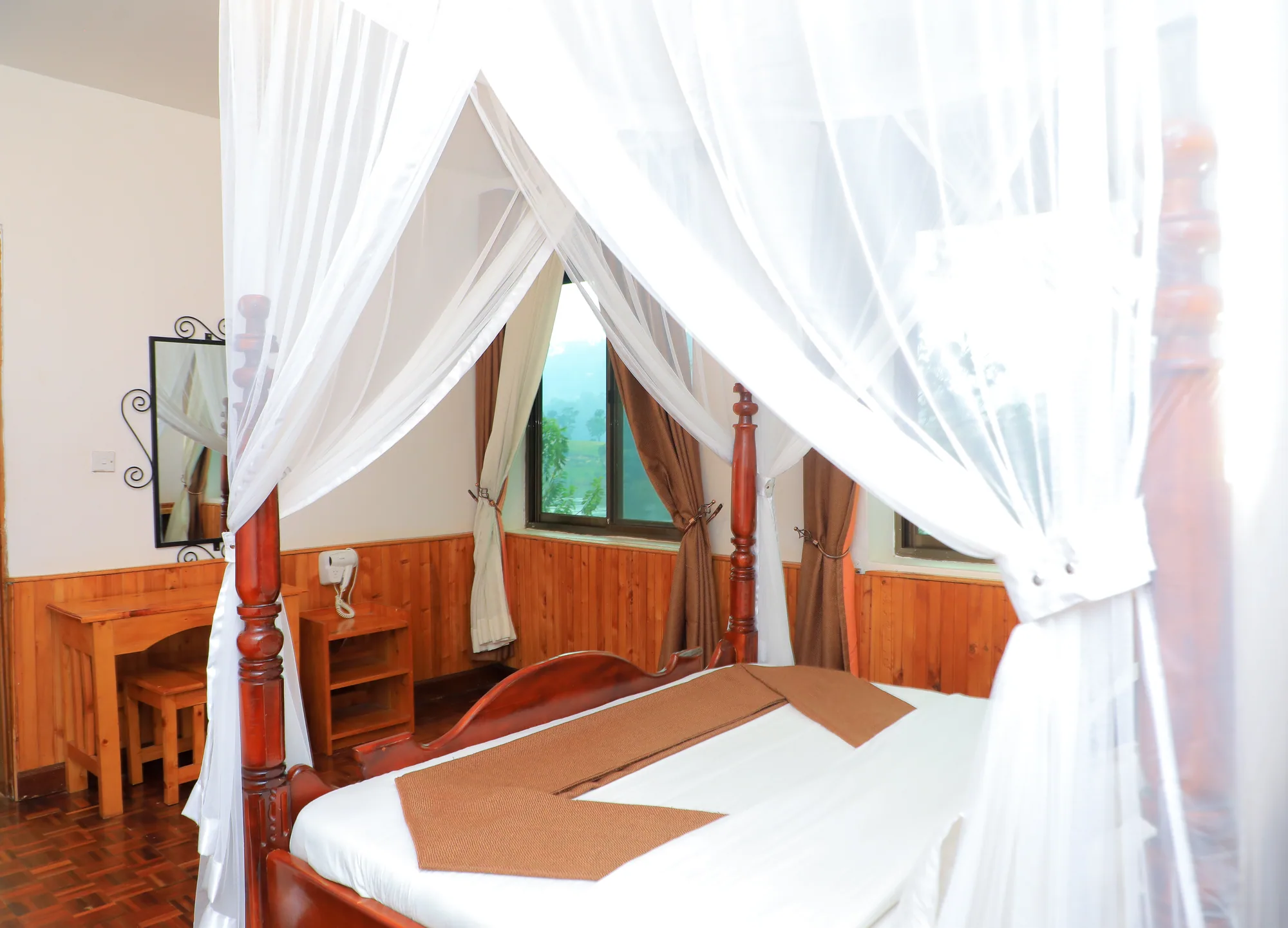 Cottage: four-poster bed under an open mosquito net in a panelled room with a desk