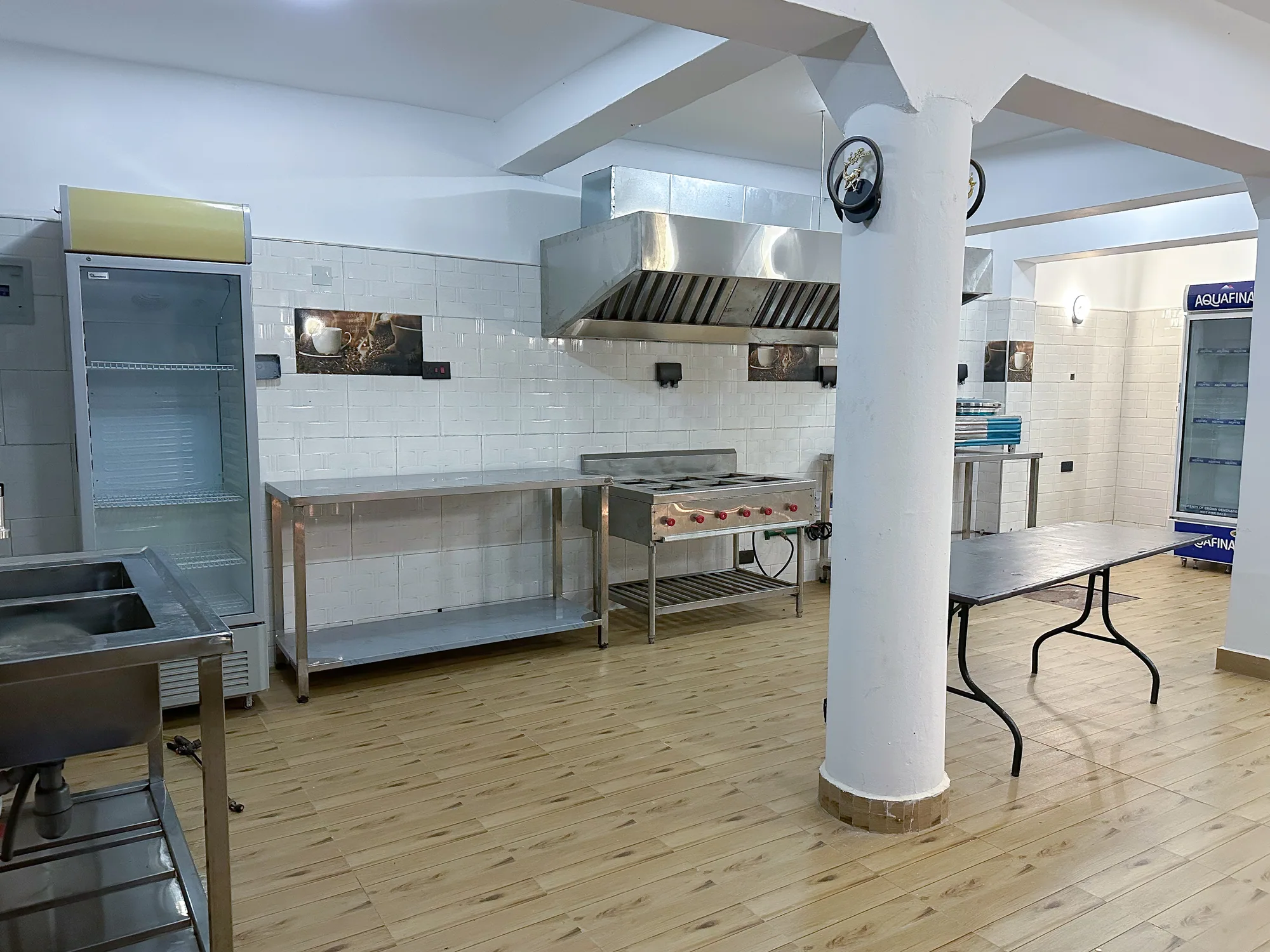 An empty commercial kitchen with steel benches, cooker and hood beside a white column
