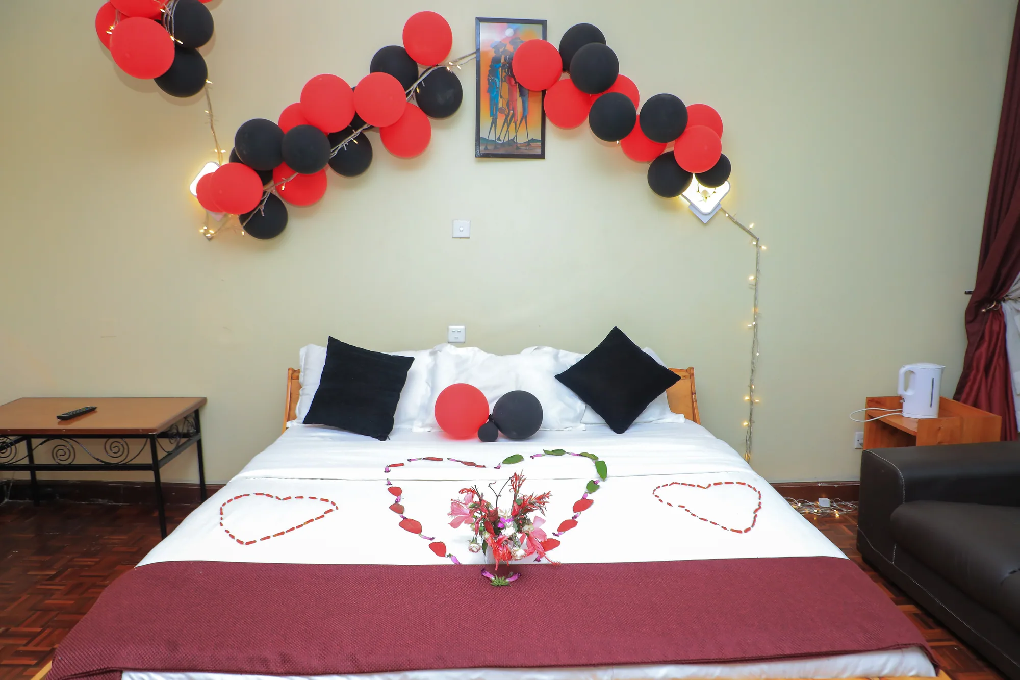 Deluxe Triple Room: bed set with rose petals in heart shapes under a red and black balloon arch