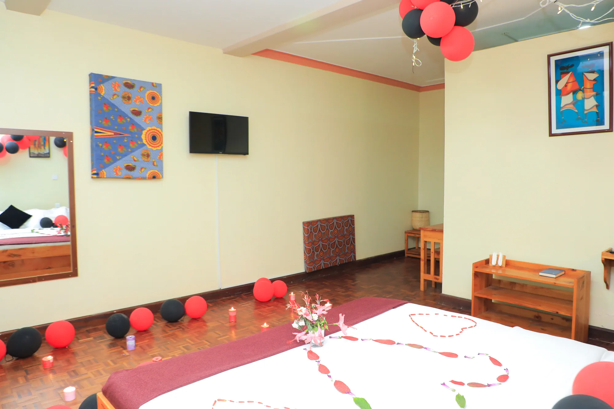 Deluxe Triple Room: celebration room with balloons along the floor, petals on the bed and a wall-mounted screen