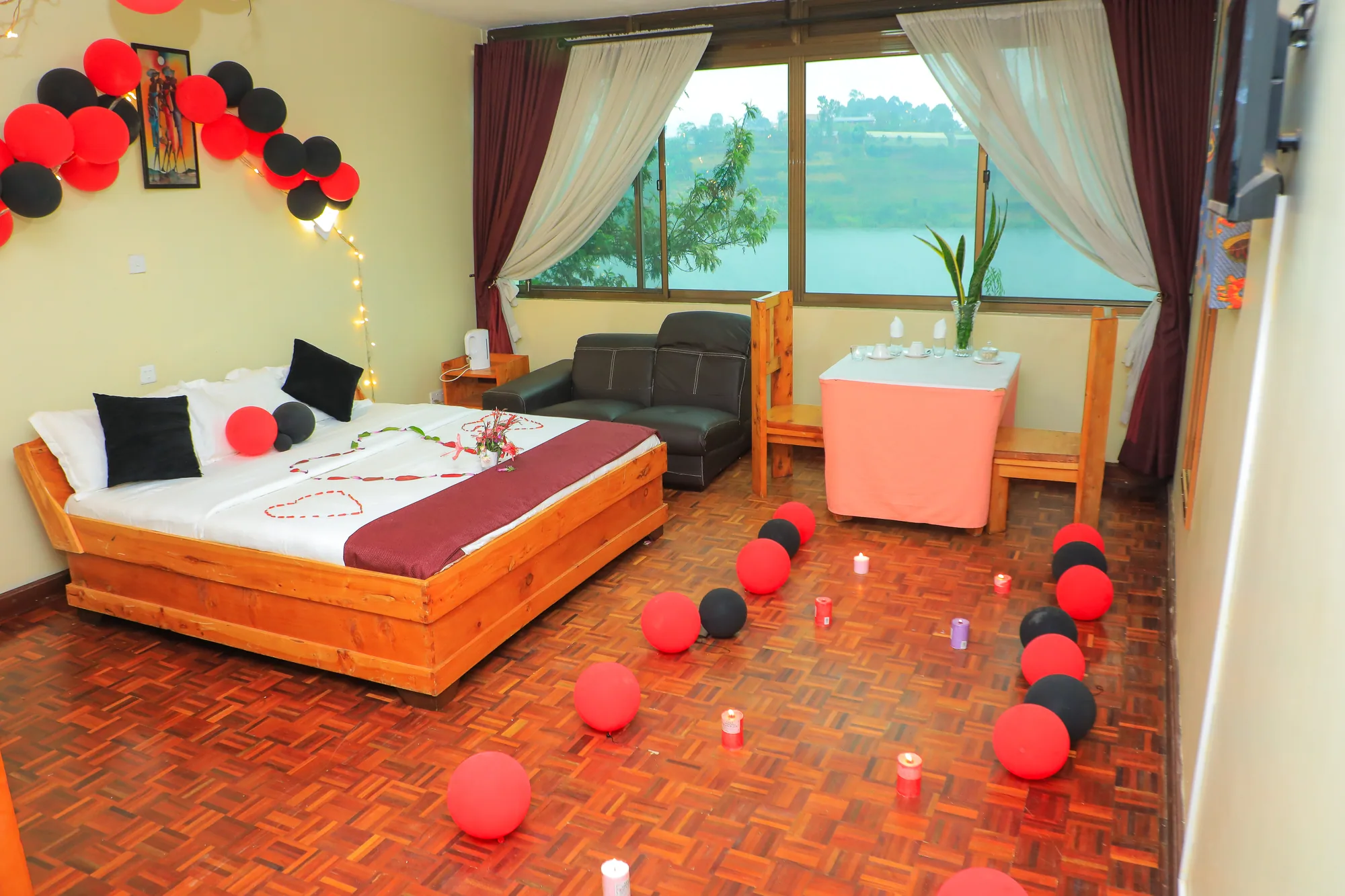 Deluxe Triple Room: bed with a maroon runner beside a picture window, balloons and candles on the floor