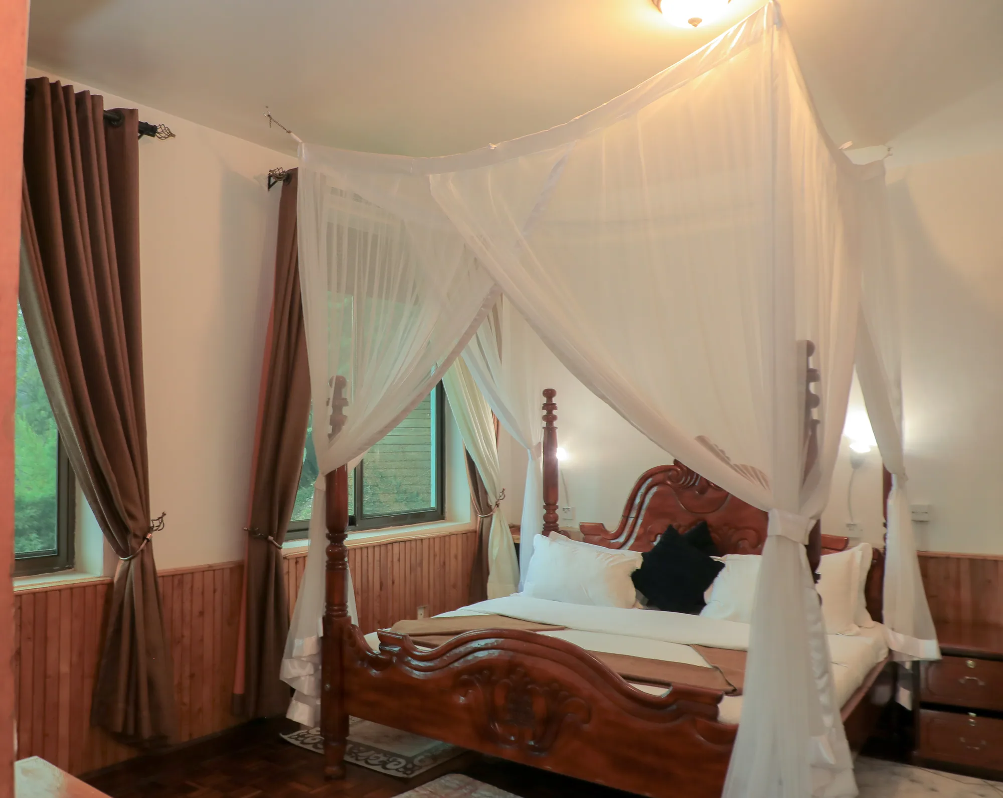 Cottage: carved four-poster bed with an open mosquito net and maroon curtains