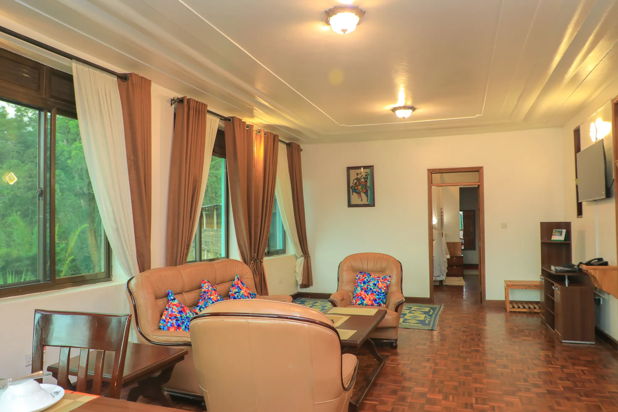 A suite bedroom with an armchair seating corner and a doorway through to the next room