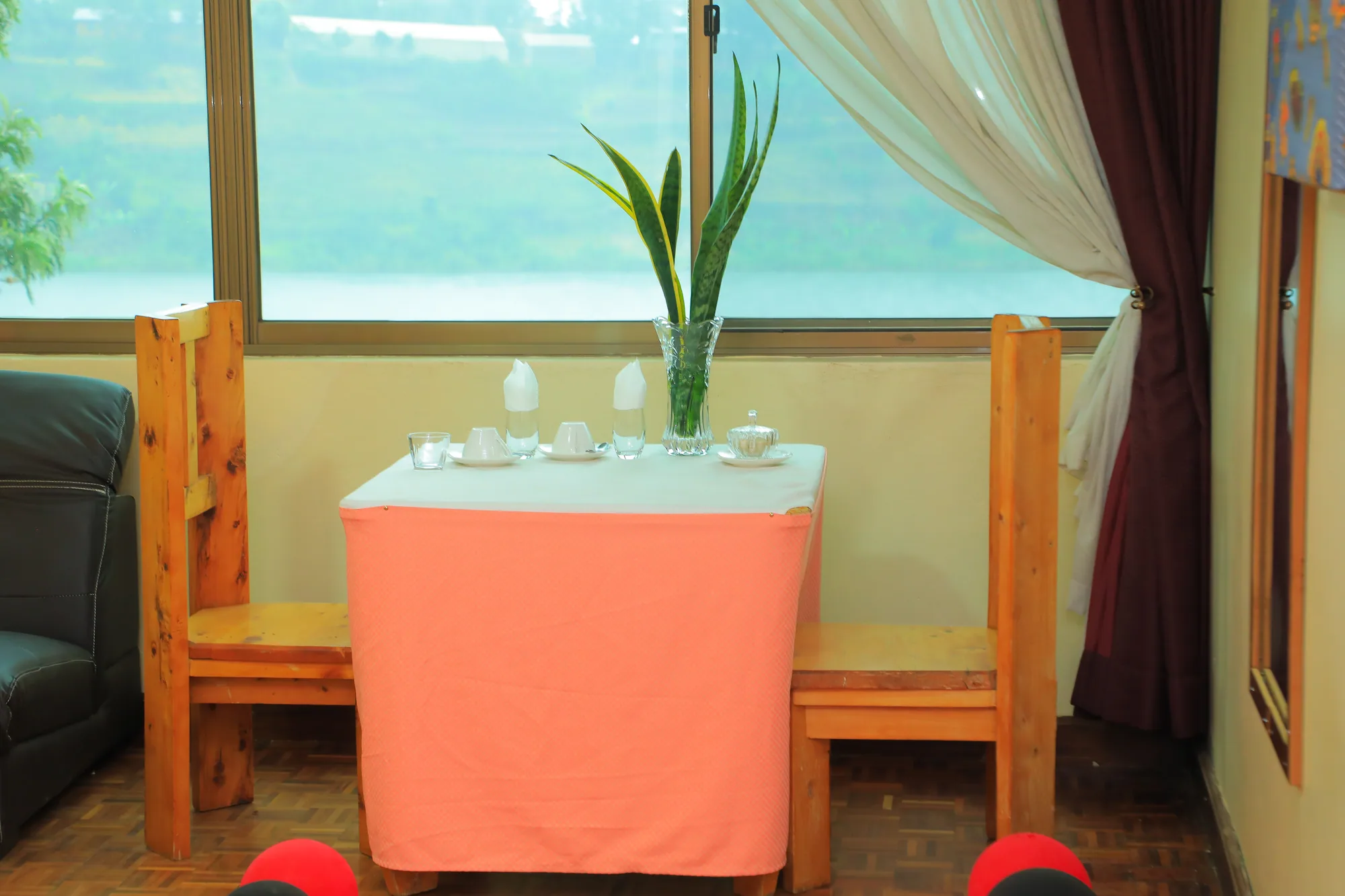 A table laid with a pink cloth, a plant and glasses in front of a lake-facing window