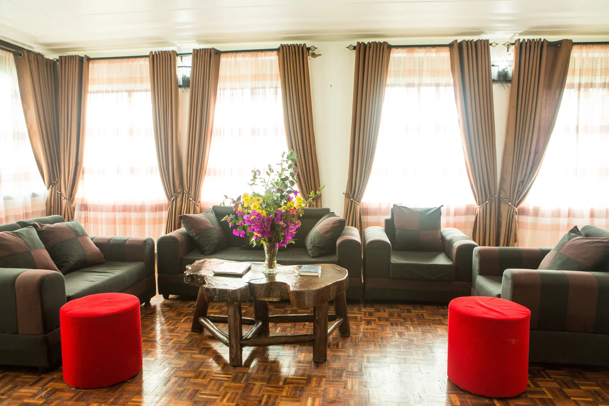 Family Suite: suite sitting room with grey sofas, red stools and a low table under tall curtained windows