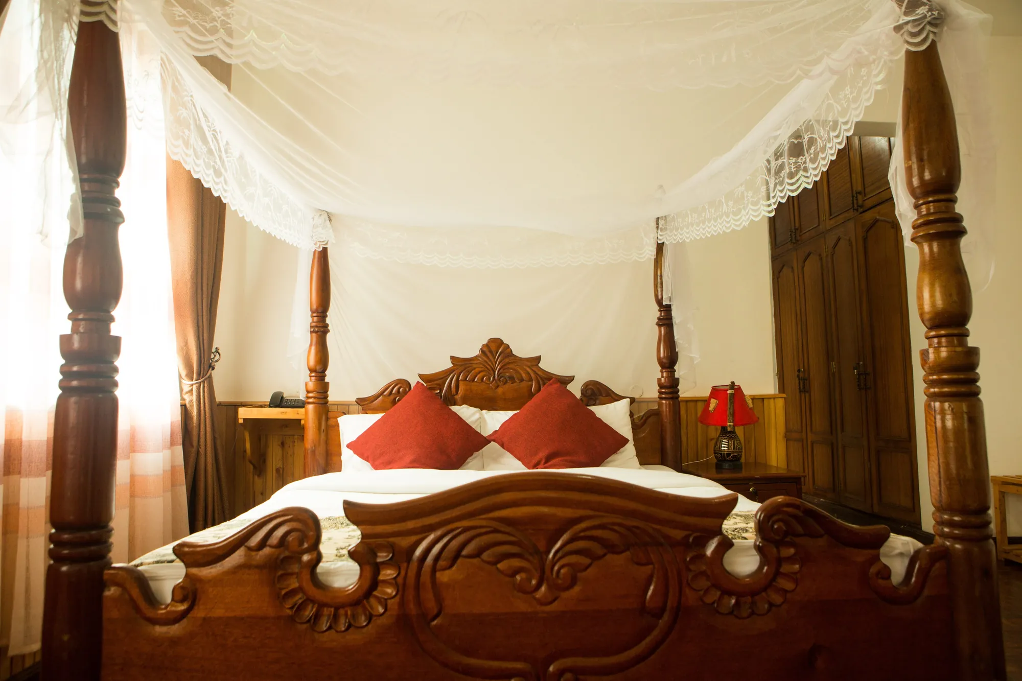 Family Suite four-poster bed draped with white mosquito netting against timber-panelled walls