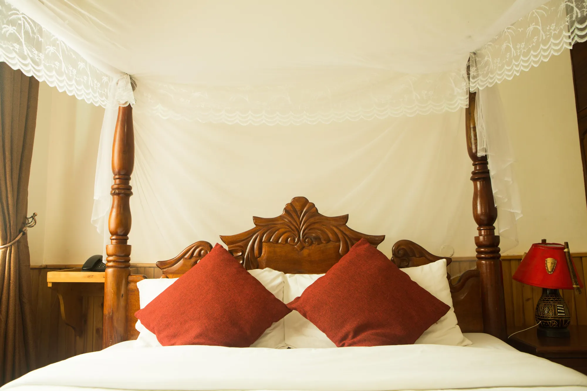 Family Suite: carved bed with red cushions under an open mosquito net, a bedside lamp alongside